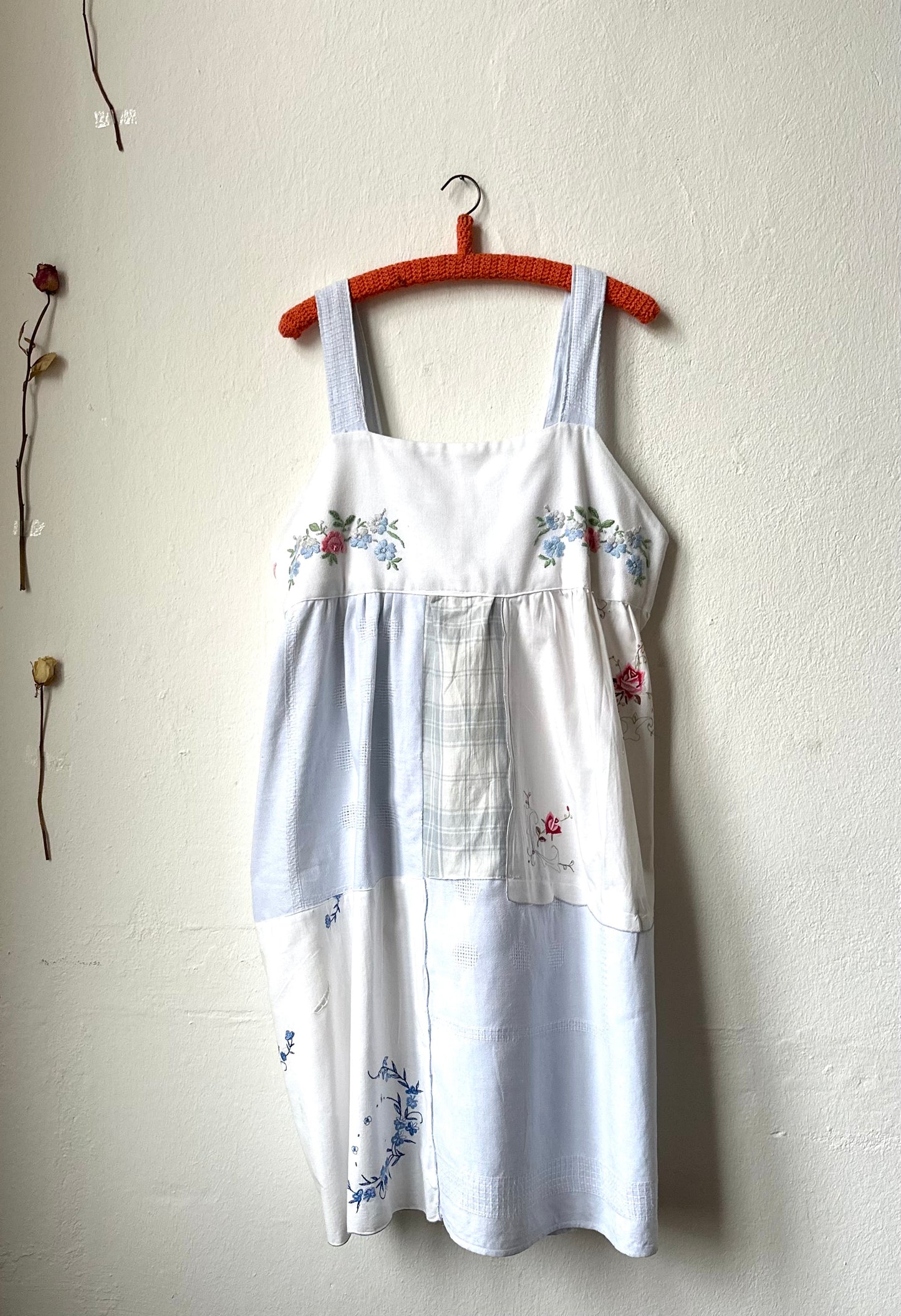A Blue and White embroidered patchwork dress hangs on a wall.