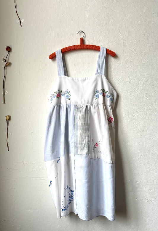 A Blue and White embroidered patchwork dress hangs on a wall.