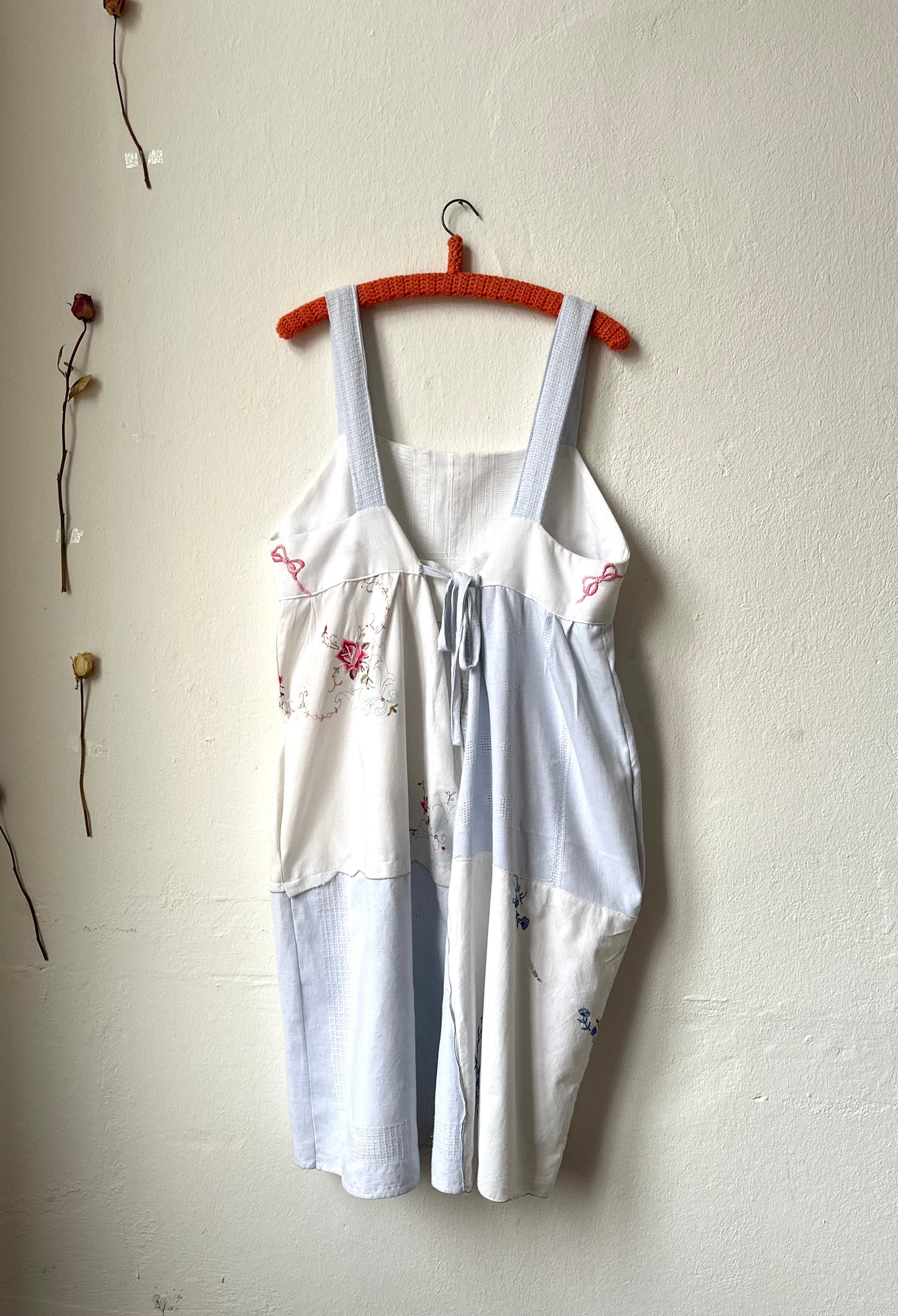 Back view of a blue and white patchwork embroidered dress hanging on the wall