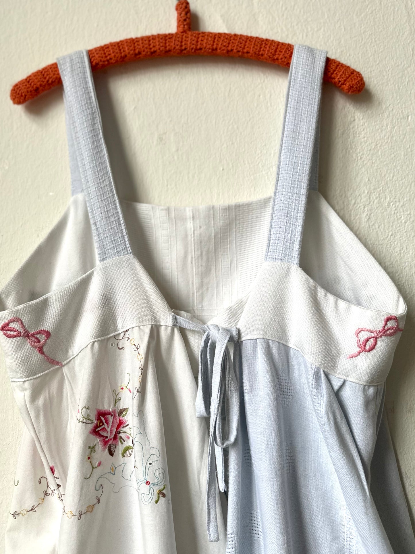 A detail view of the back of a white and blue embroidered dress hanging on a wall