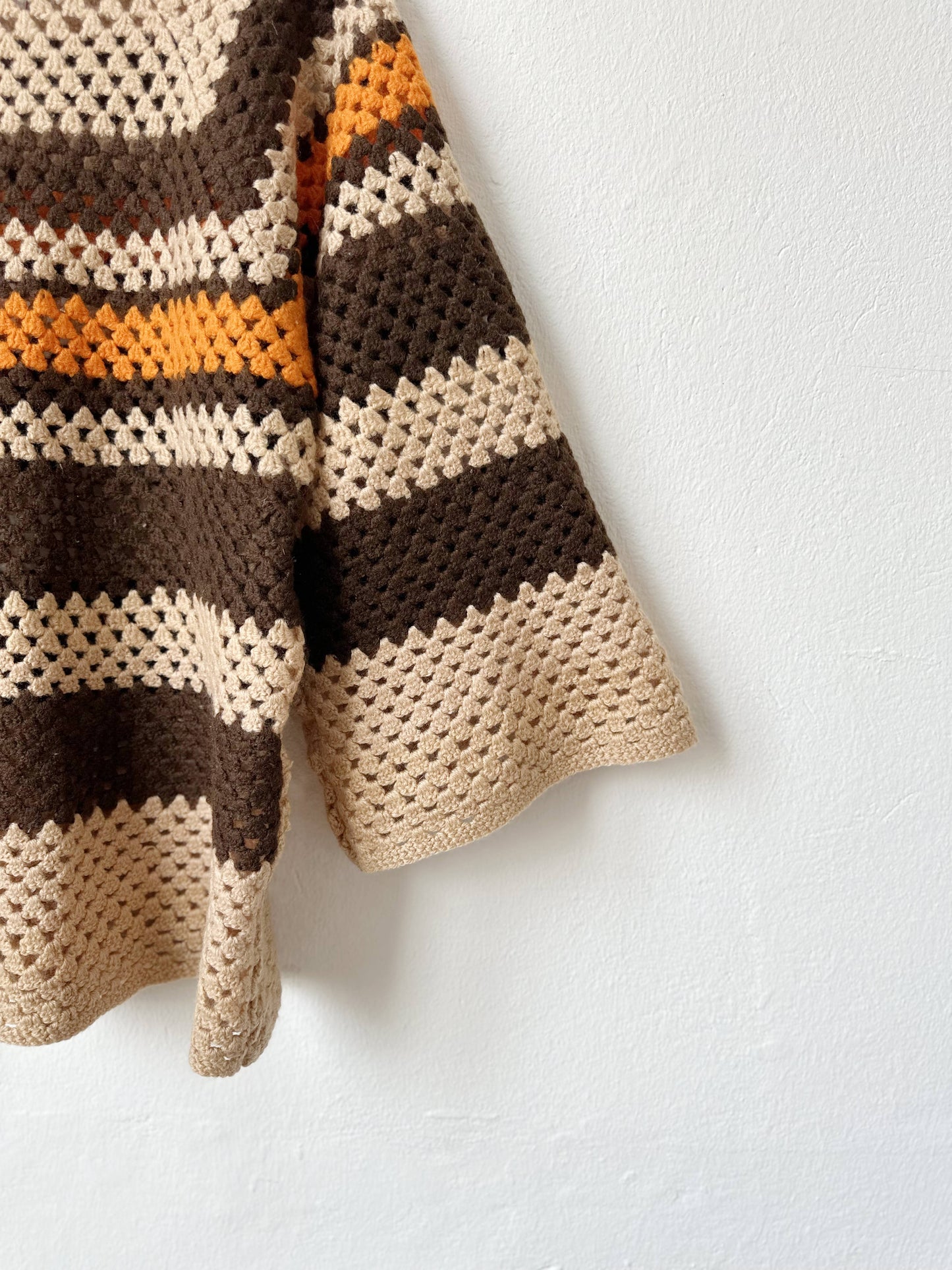 A detail sleeve view of a brown striped sweater hanging on a wall