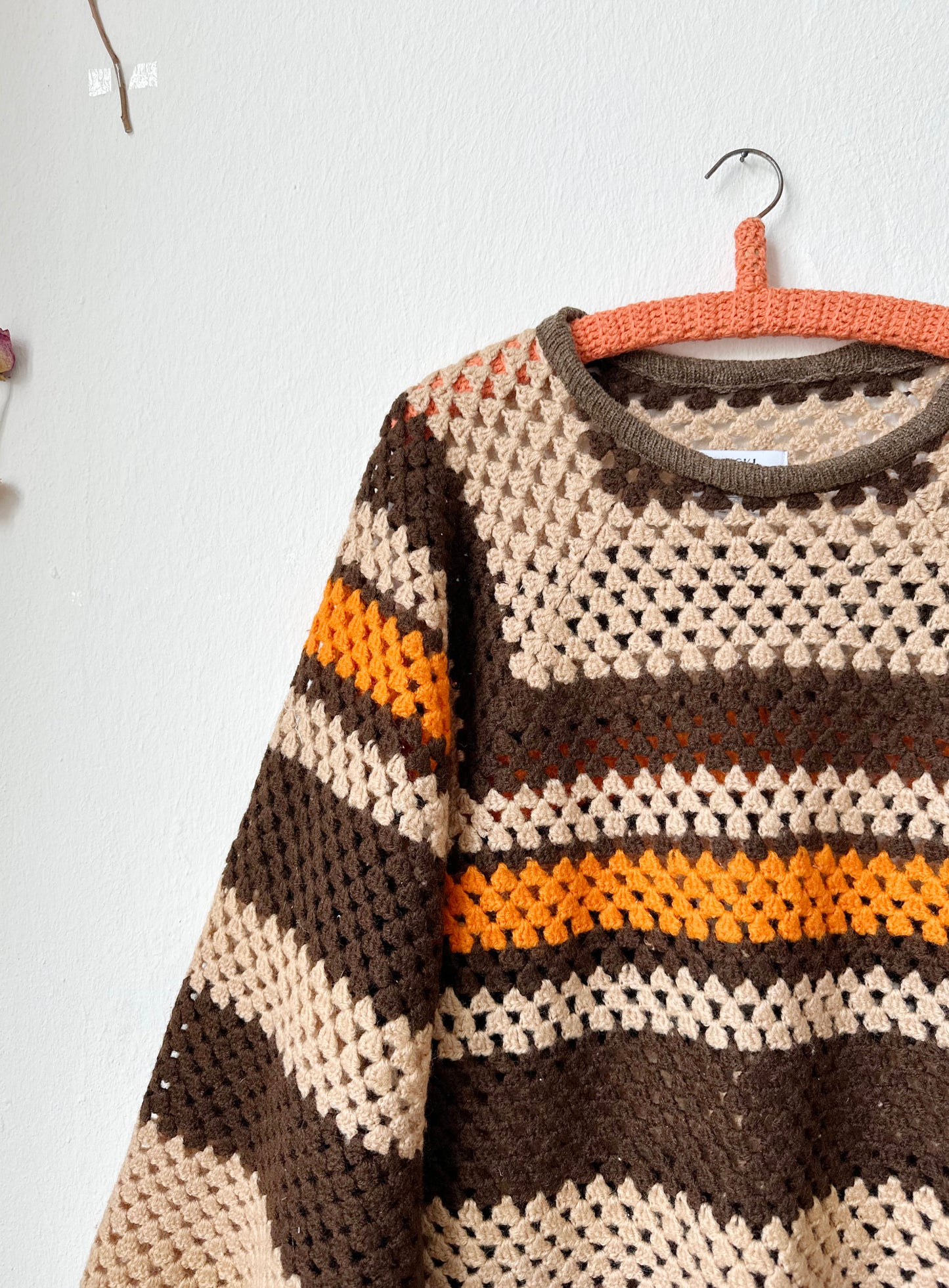 A detail front view of a brown stripe sweater hanging on a wall.