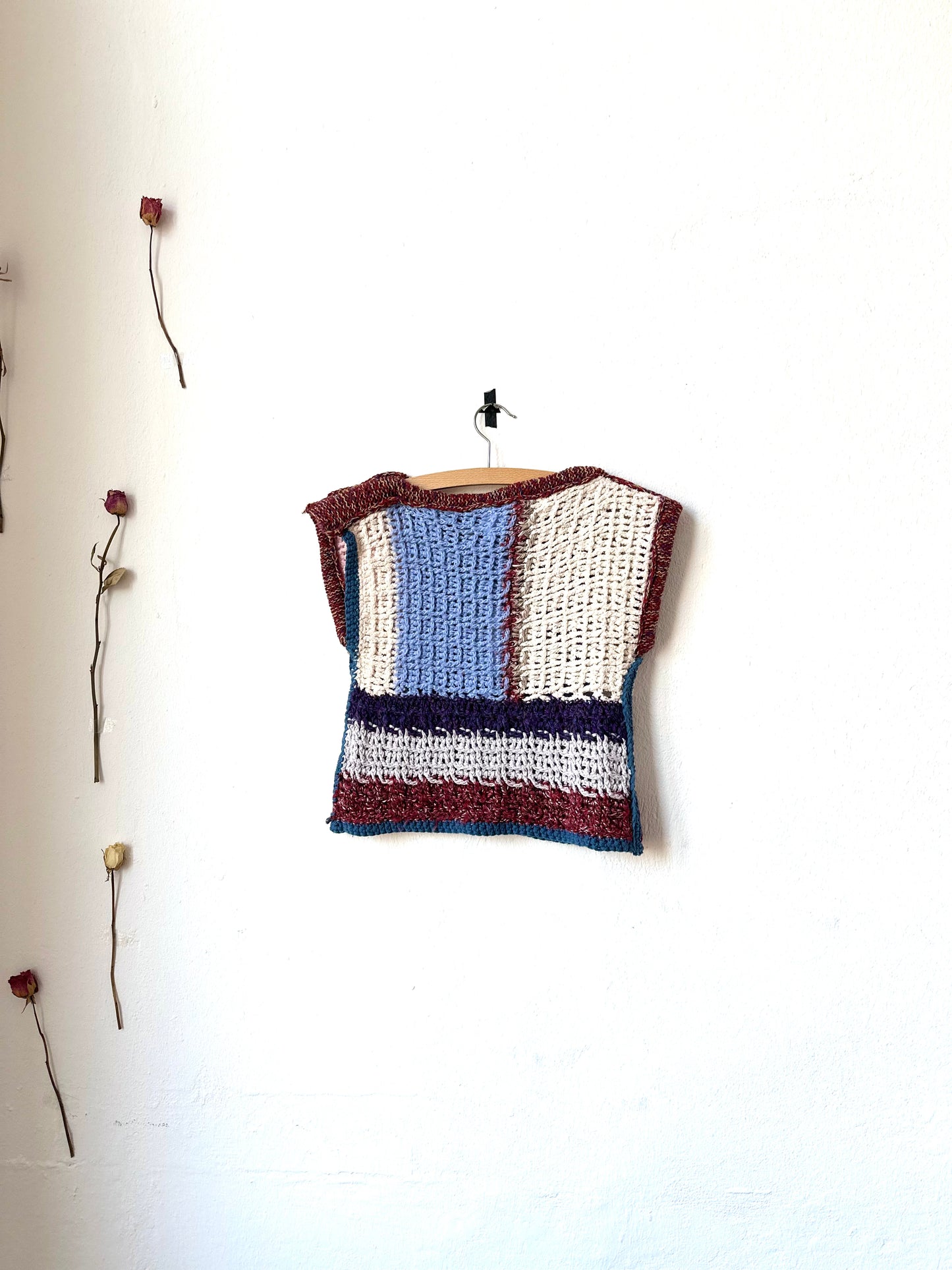 View of a crochet blanket vest hanging on a wall.