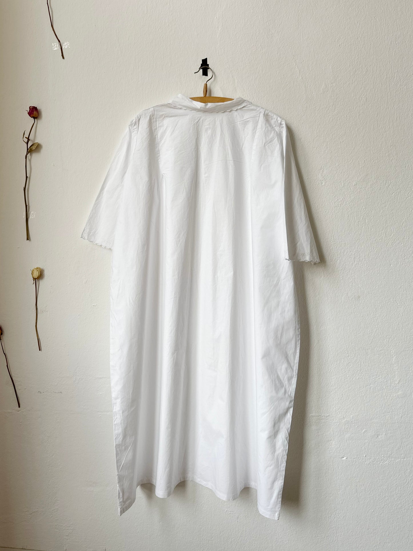 White dress hanging on a hanger against a white wall with minimal decor.