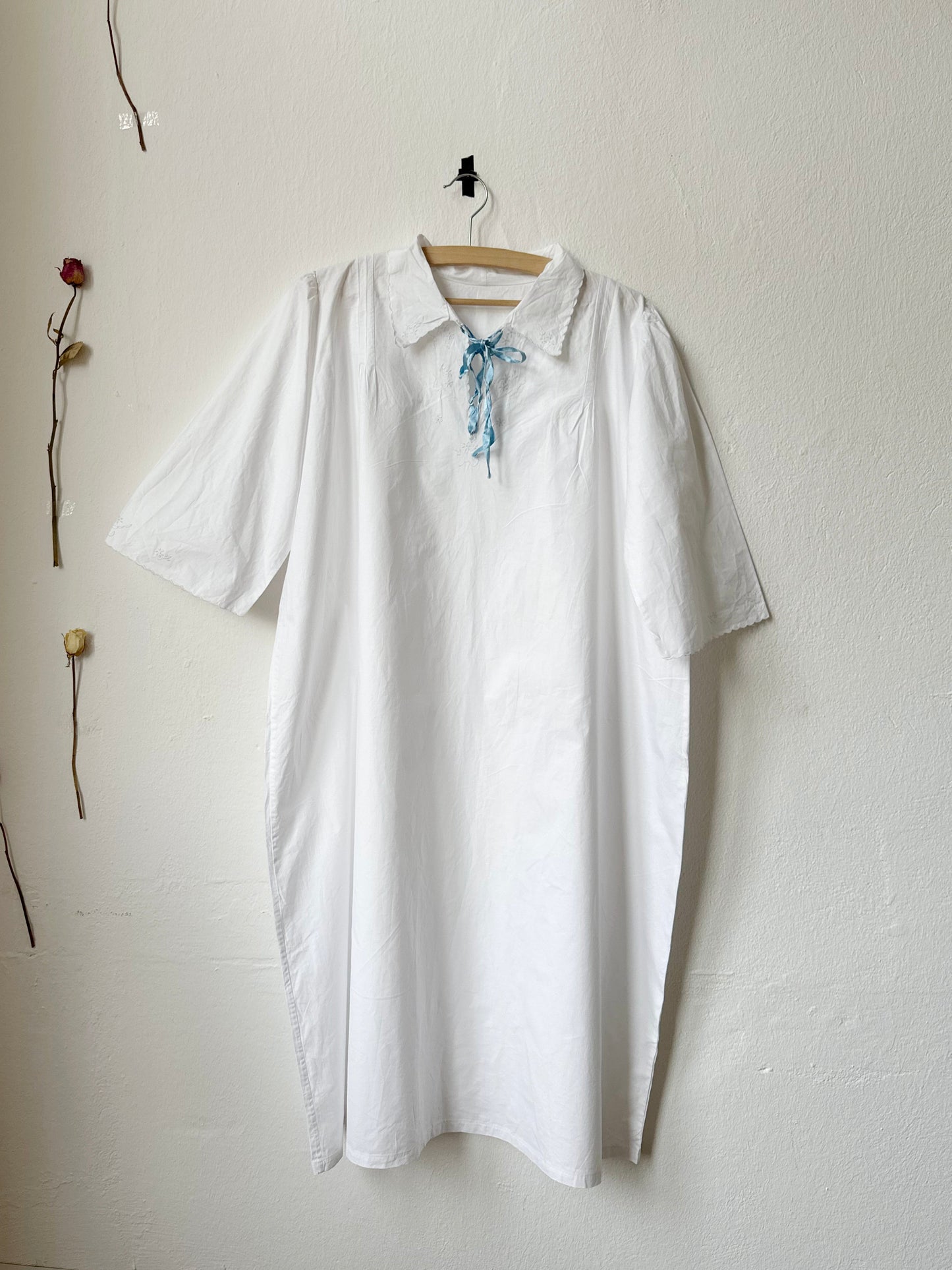 White vintage italian nightgown with blue ribbon at neck hangs on a wall.