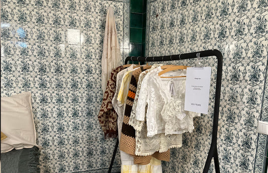 A rail of clothes sits in front of a green and white tiled wall.