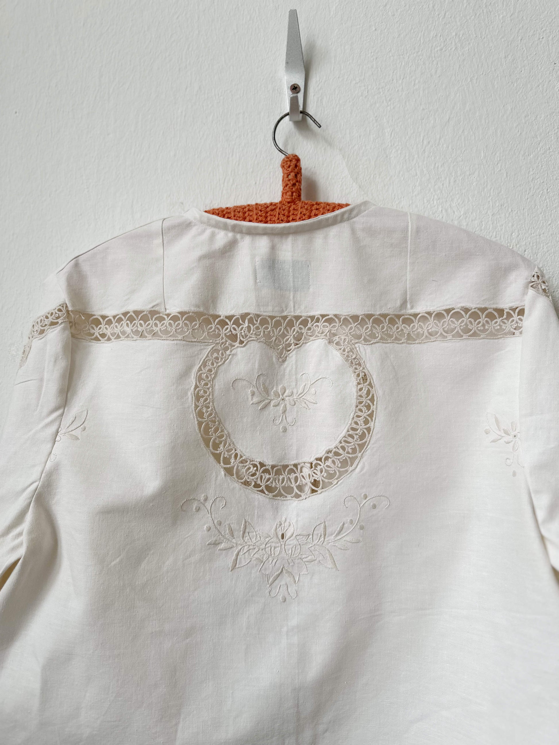 Handmade long sleeve vintage lace and embroidered cotton blouse sourced in Rome, hanging on a wall in Berlin studio