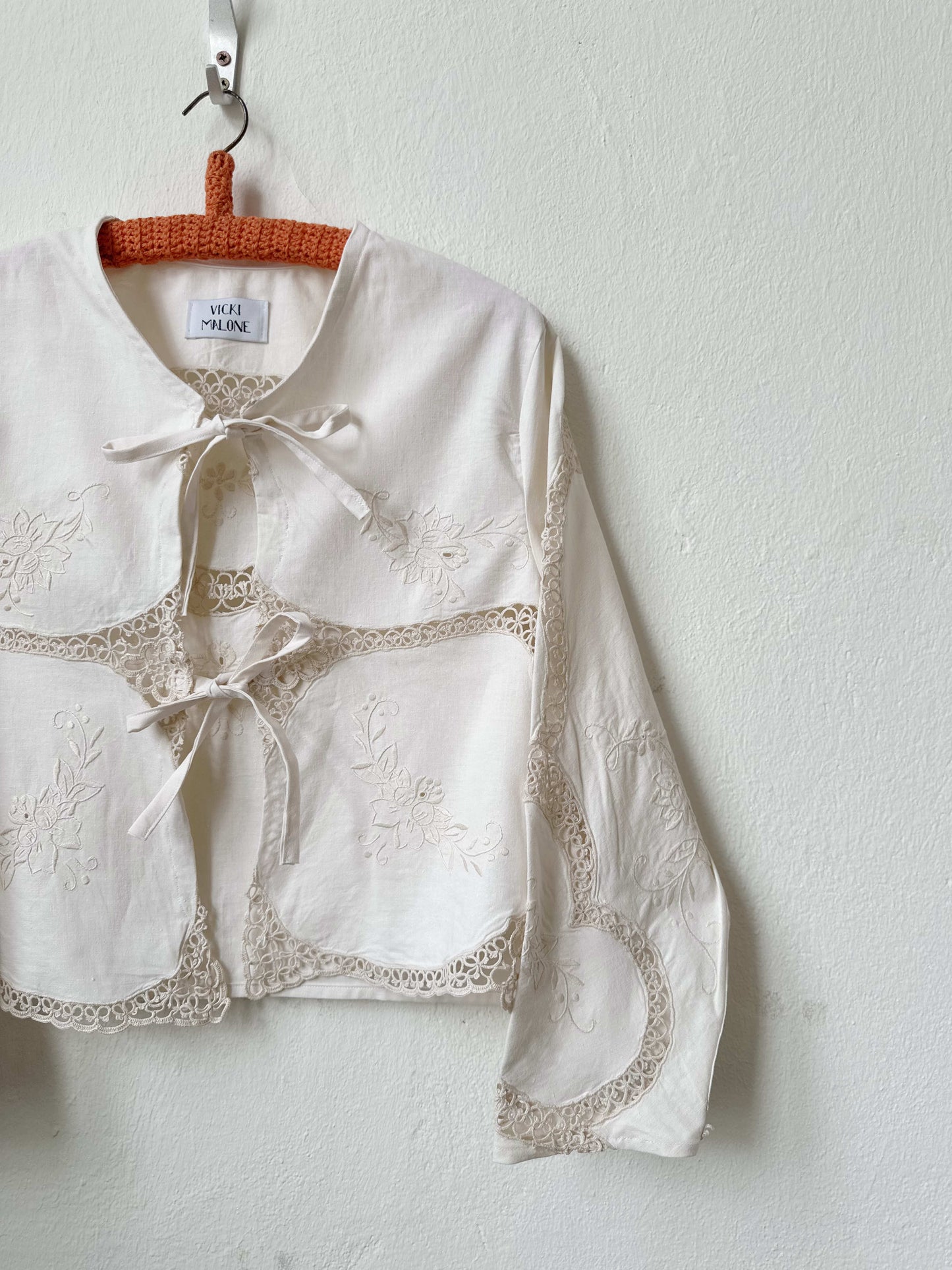 Handmade long sleeve vintage lace and embroidered cotton blouse sourced in Rome, hanging on a wall in Berlin studio