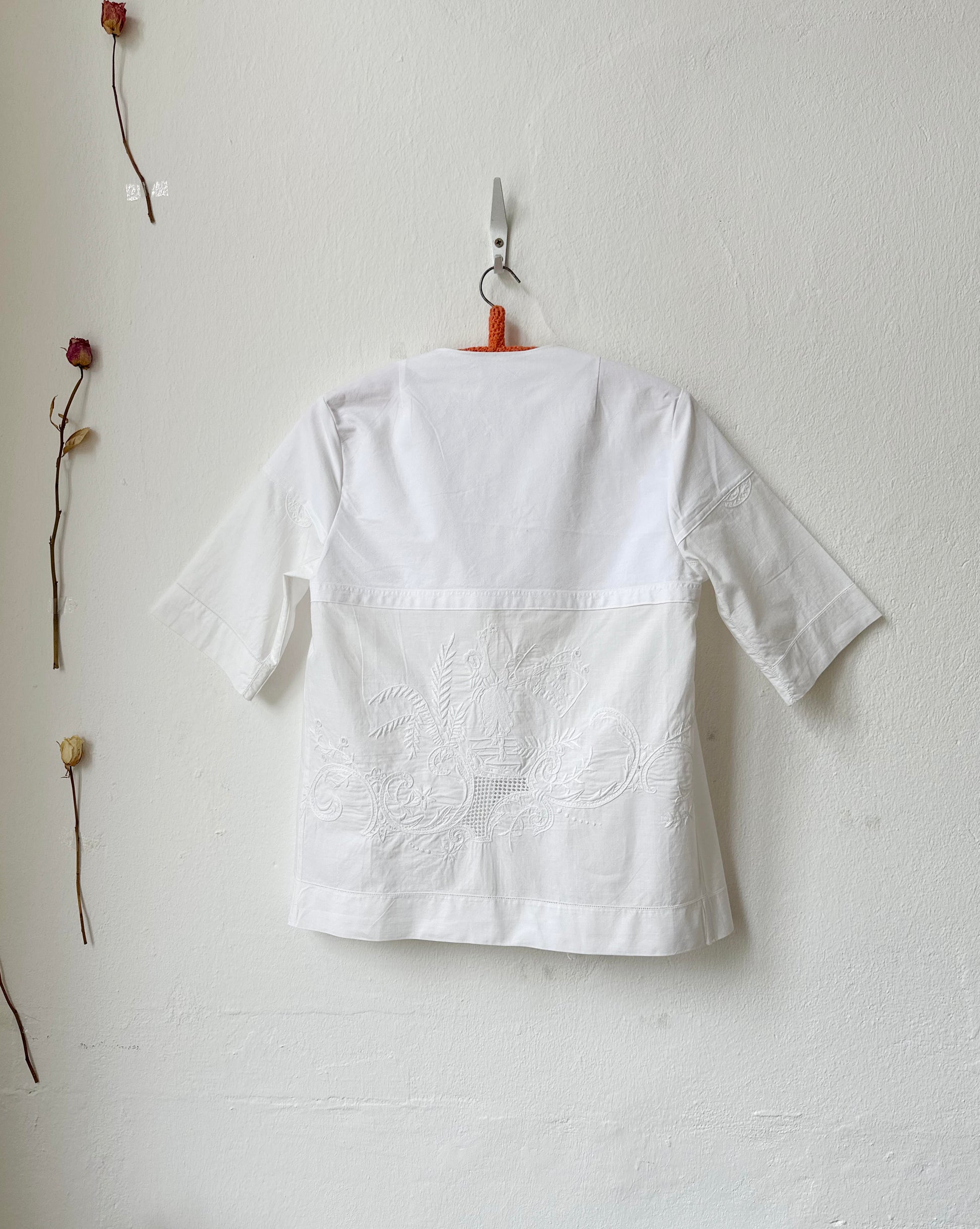 White shirt hanging on a white wall with dried flowers.