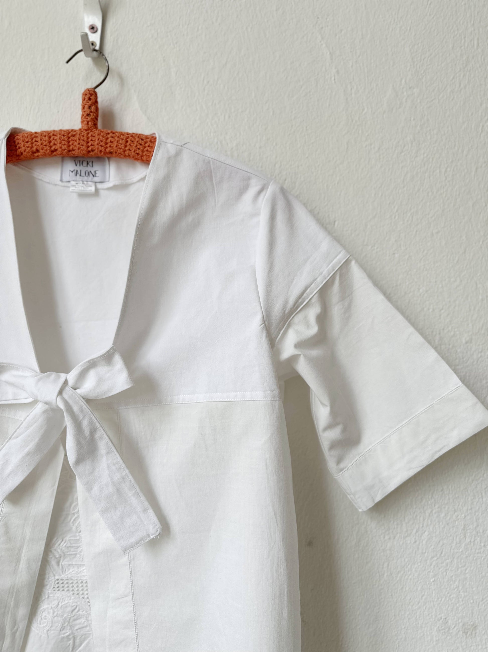 White blouse with a tie hanging on an orange hanger against a white wall.