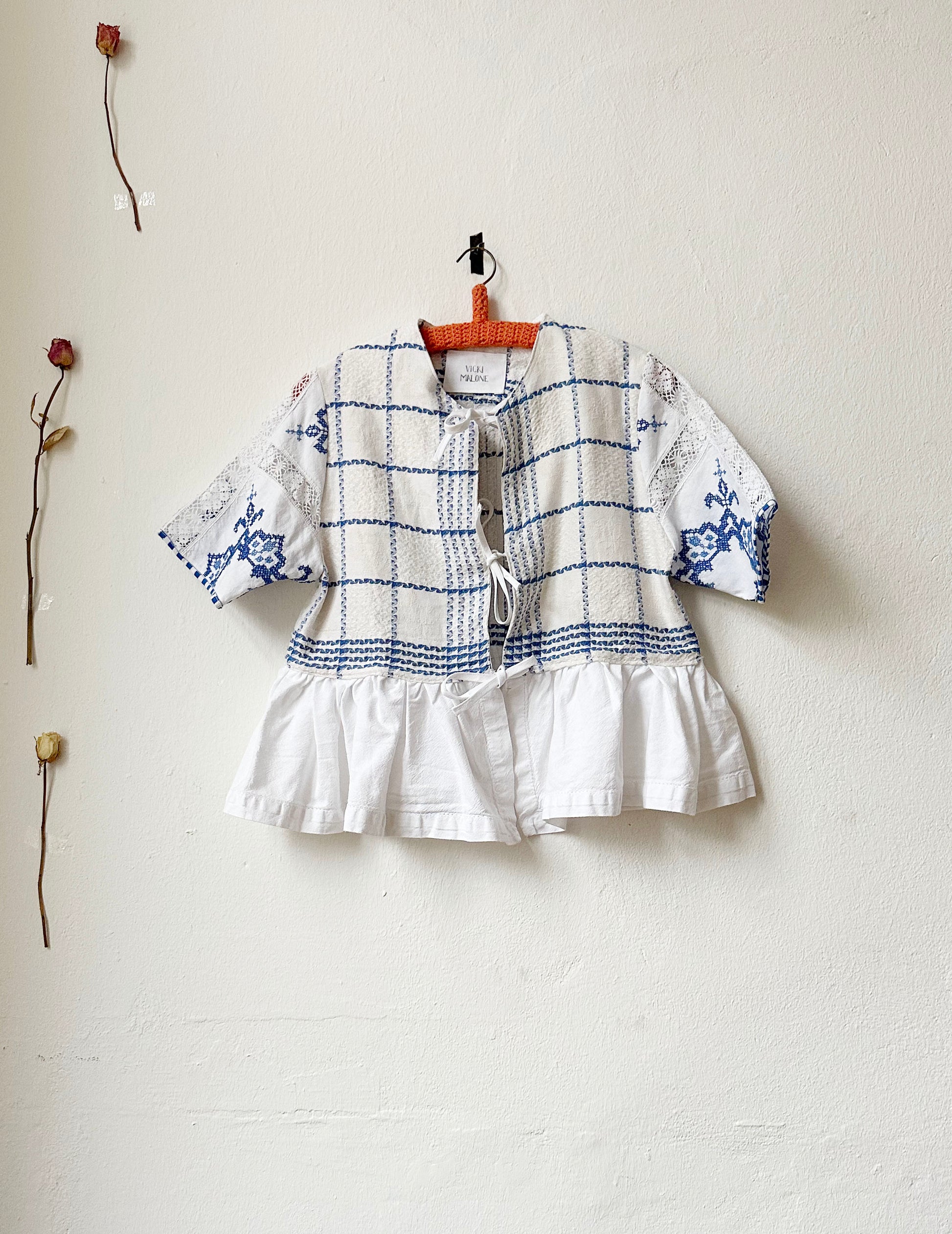 A blue and white check blouse with tie closure and peplum hem hanging on a wall. 