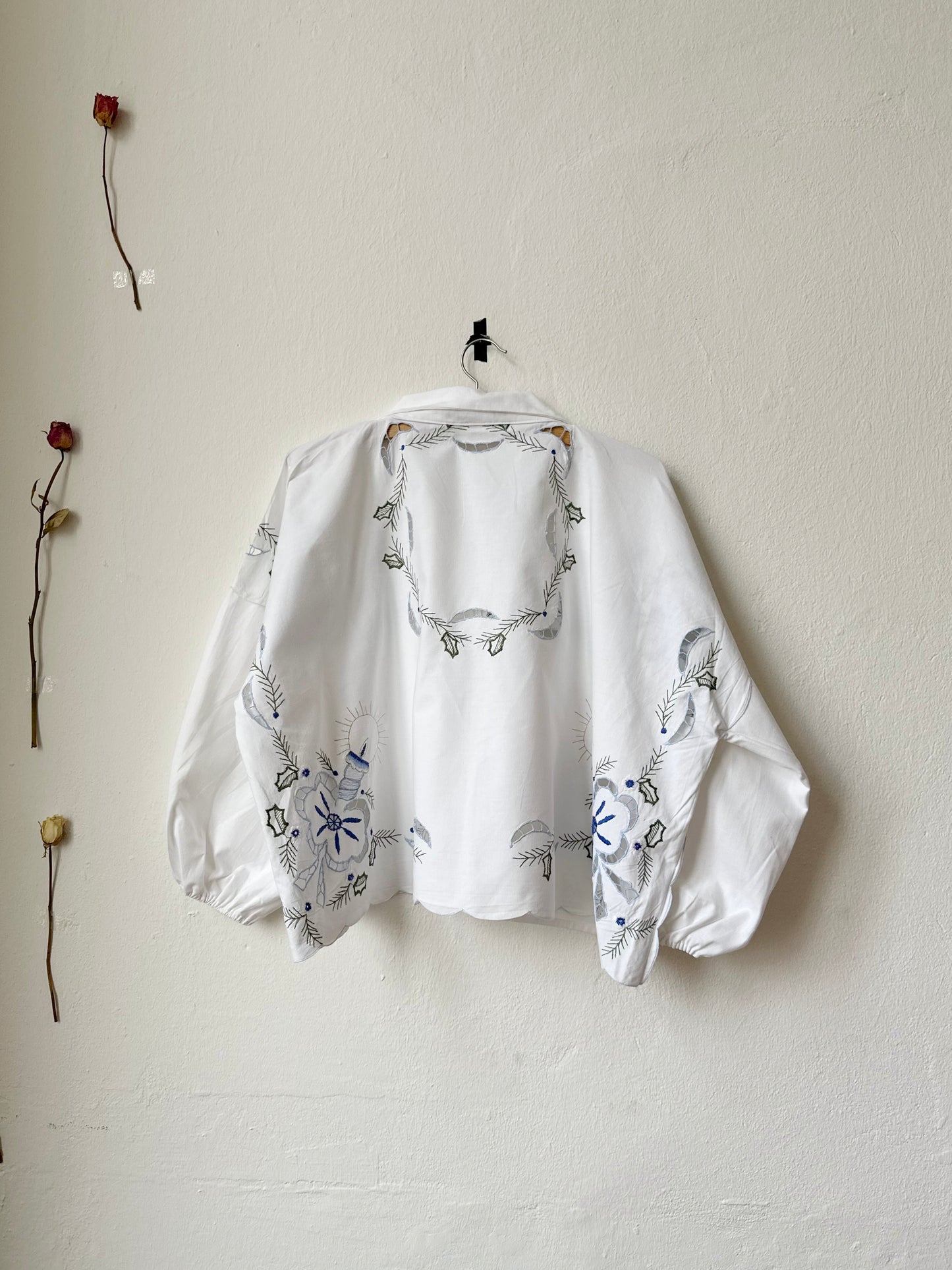 Back view of an embroidered white blouse hanging on a wall.