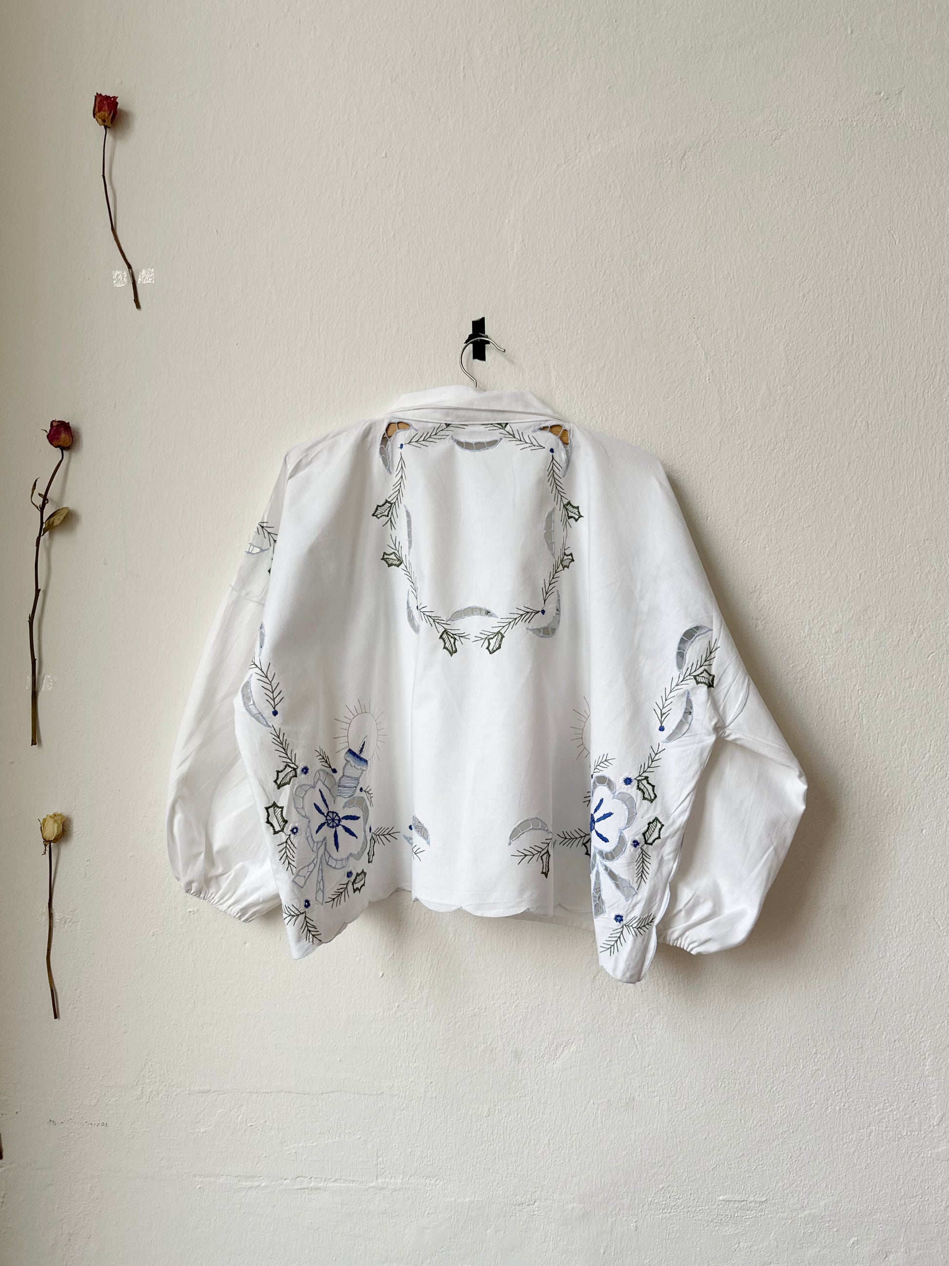 Back view of an embroidered white blouse hanging on a wall.