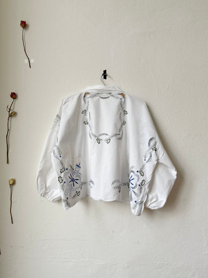 Back view of an embroidered white blouse hanging on a wall.