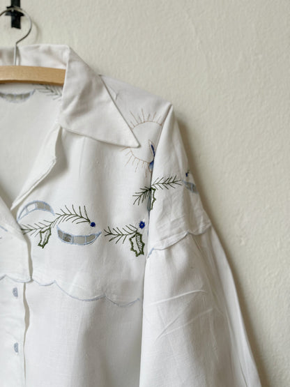A detail view of the embroidery of a white blouse hanging on a wall.