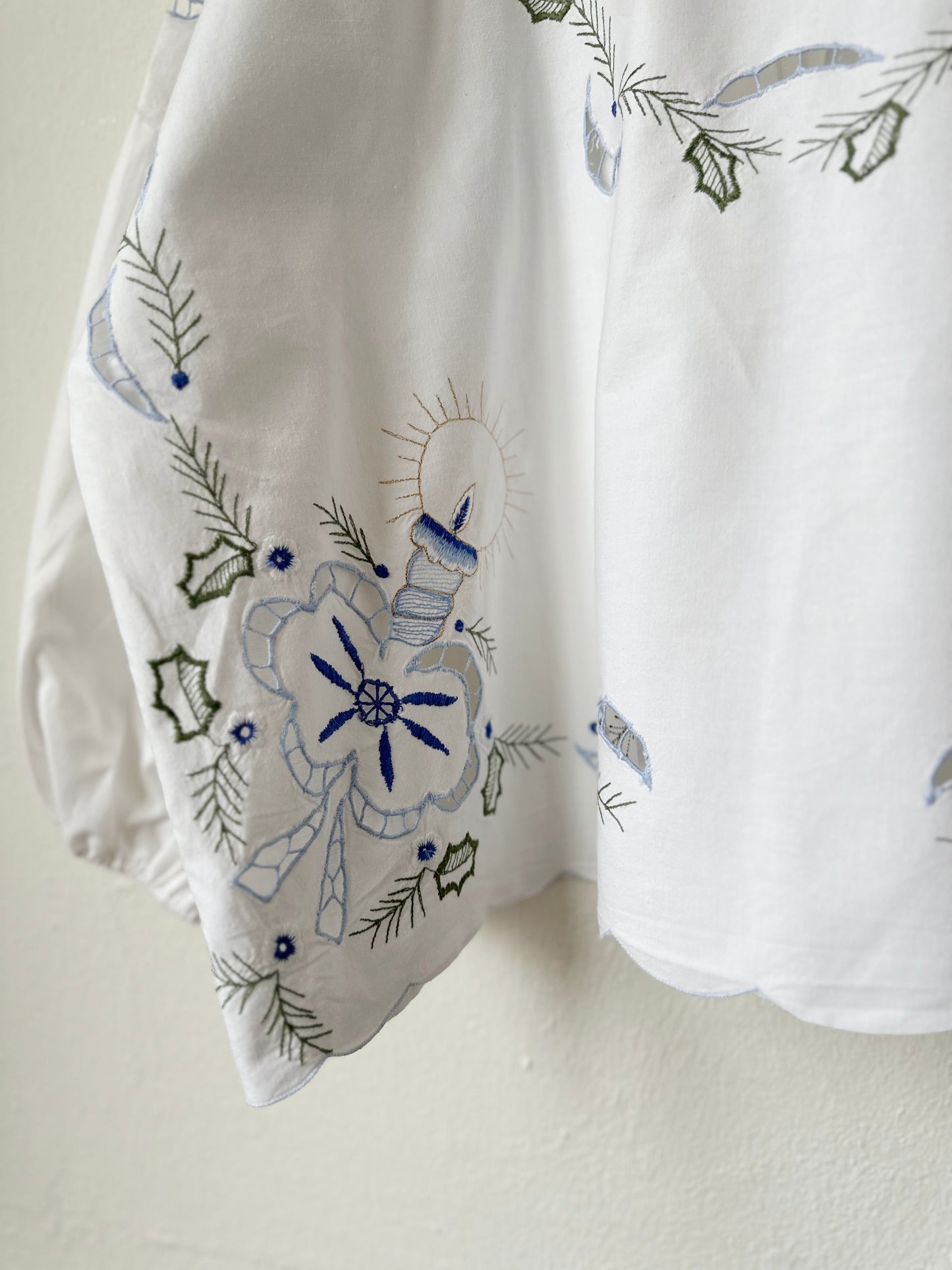 Embroidery detail of blouse hanging on a wall.