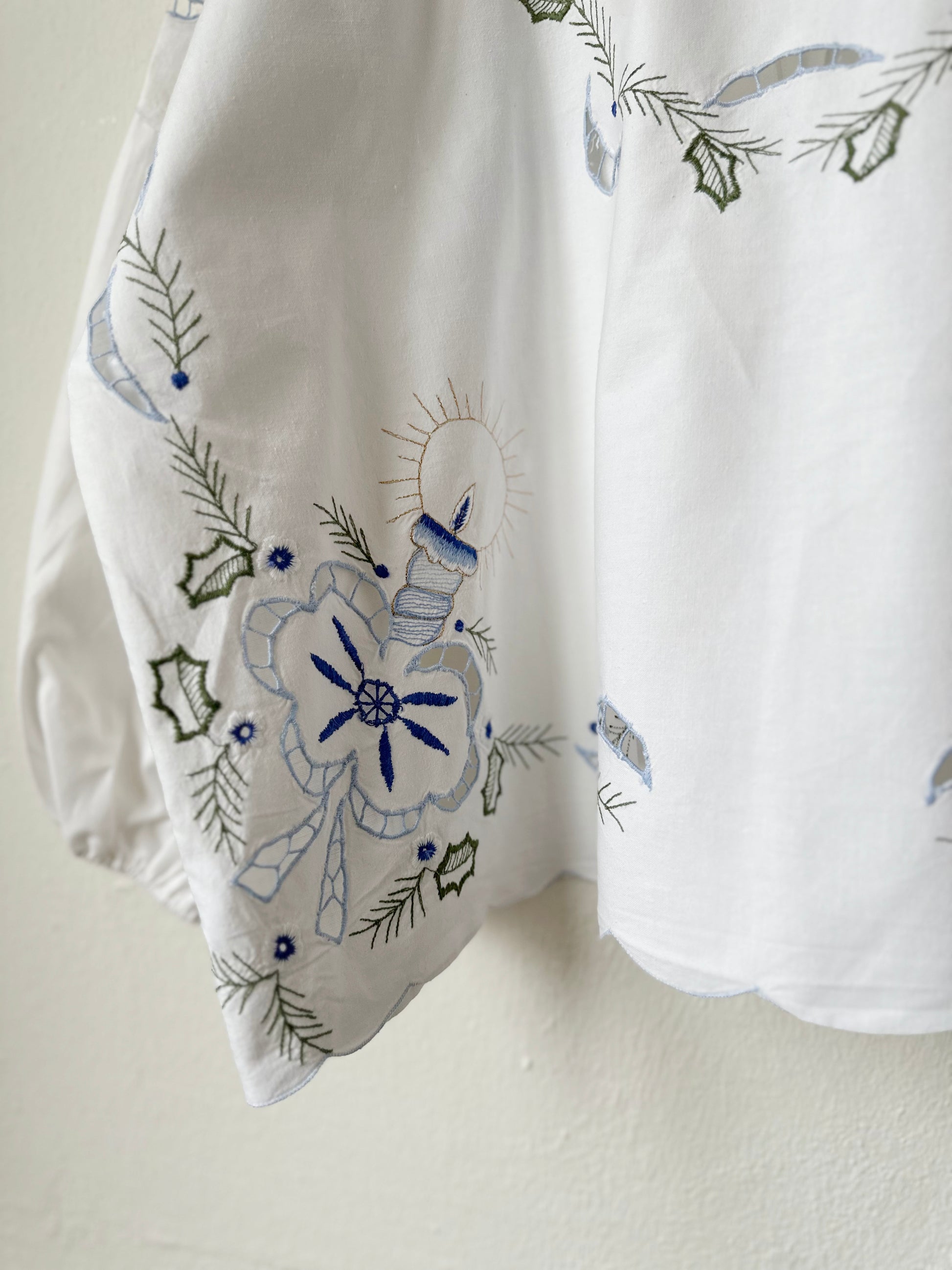 Embroidery detail of blouse hanging on a wall.