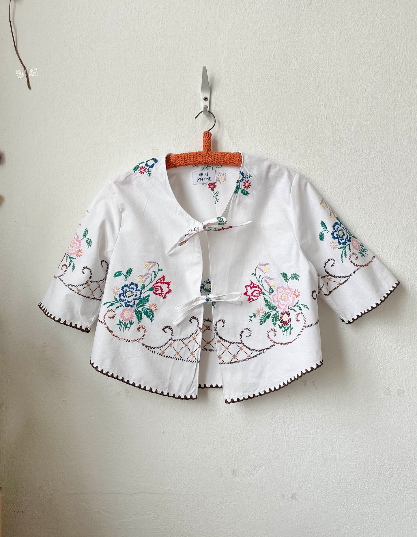 Handmade short sleeve embroidered cotton blouse made from a vintage Berlin flea market tablecloth, hanging on a wall
