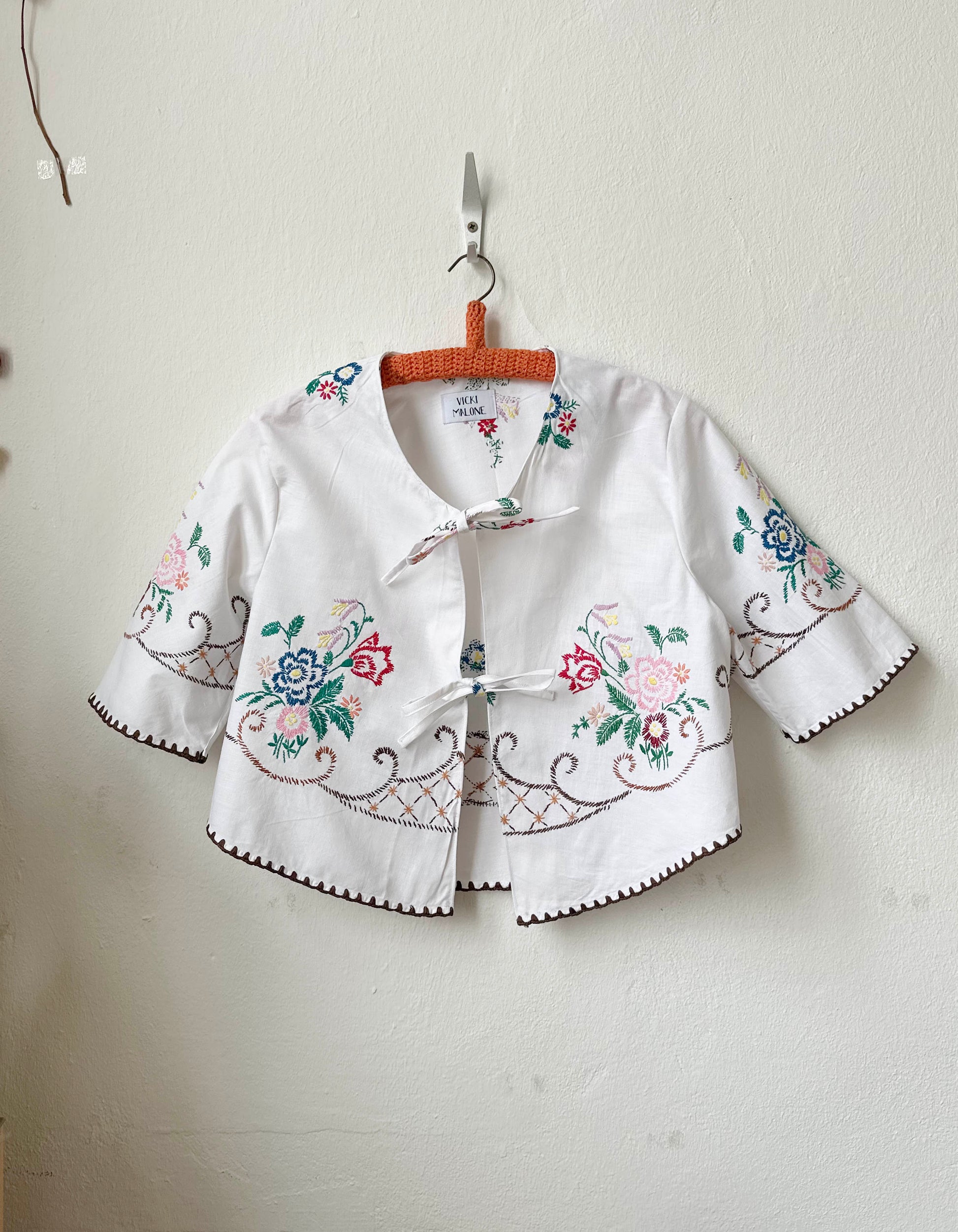 Handmade short sleeve embroidered cotton blouse made from a vintage Berlin flea market tablecloth, hanging on a wall
