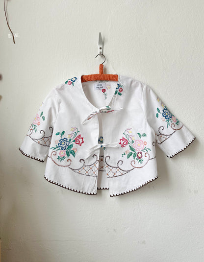 Handmade short sleeve embroidered cotton blouse made from a vintage Berlin flea market tablecloth, hanging on a wall

