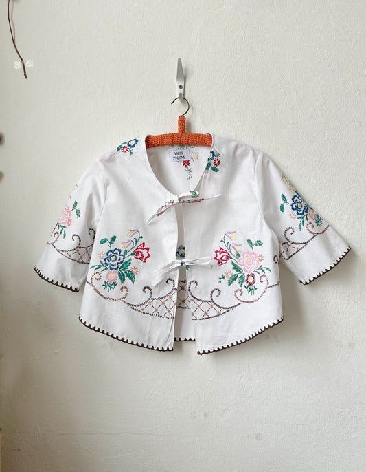 Handmade short sleeve embroidered cotton blouse made from a vintage Berlin flea market tablecloth, hanging on a wall
