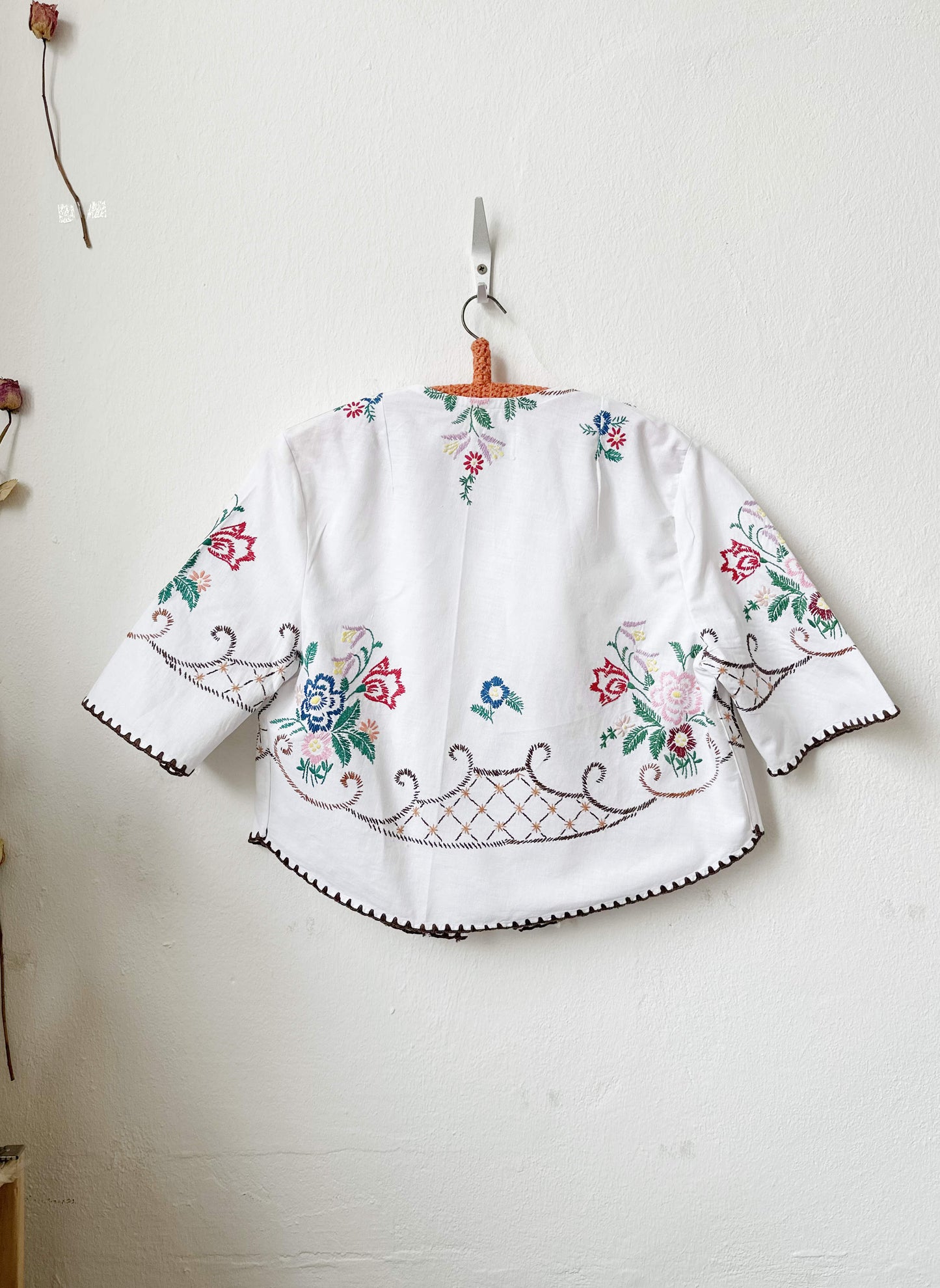 Handmade short sleeve embroidered cotton blouse made from a vintage Berlin flea market tablecloth, hanging on a wall
