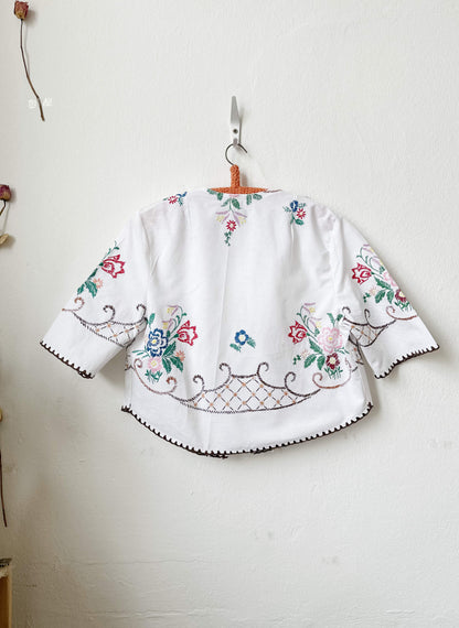 Handmade short sleeve embroidered cotton blouse made from a vintage Berlin flea market tablecloth, hanging on a wall
