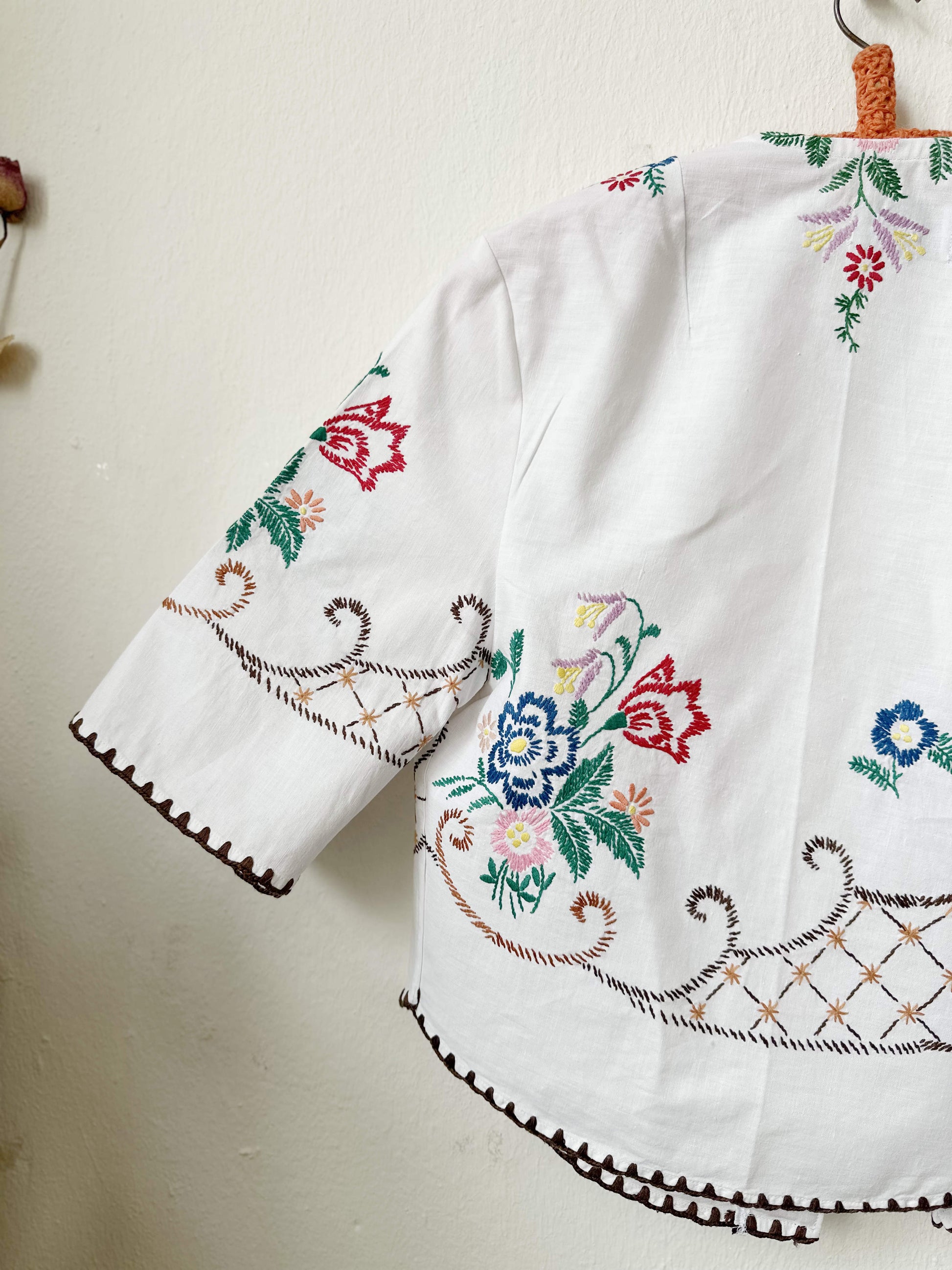 Handmade short sleeve embroidered cotton blouse made from a vintage Berlin flea market tablecloth, hanging on a wall
