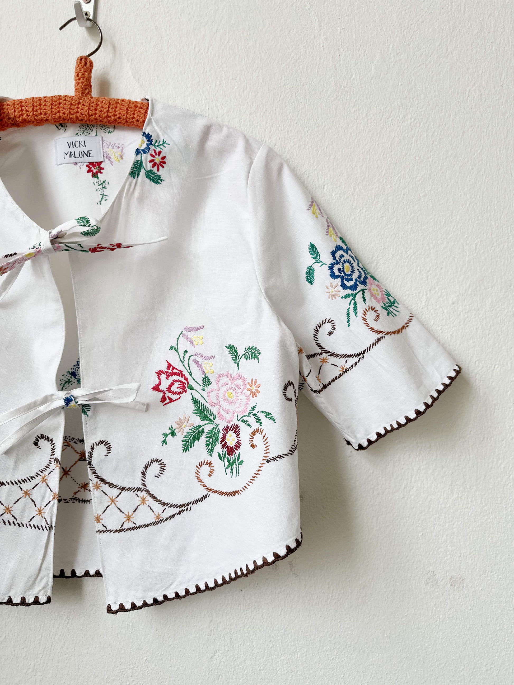 Handmade short sleeve embroidered cotton blouse made from a vintage Berlin flea market tablecloth, hanging on a wall
