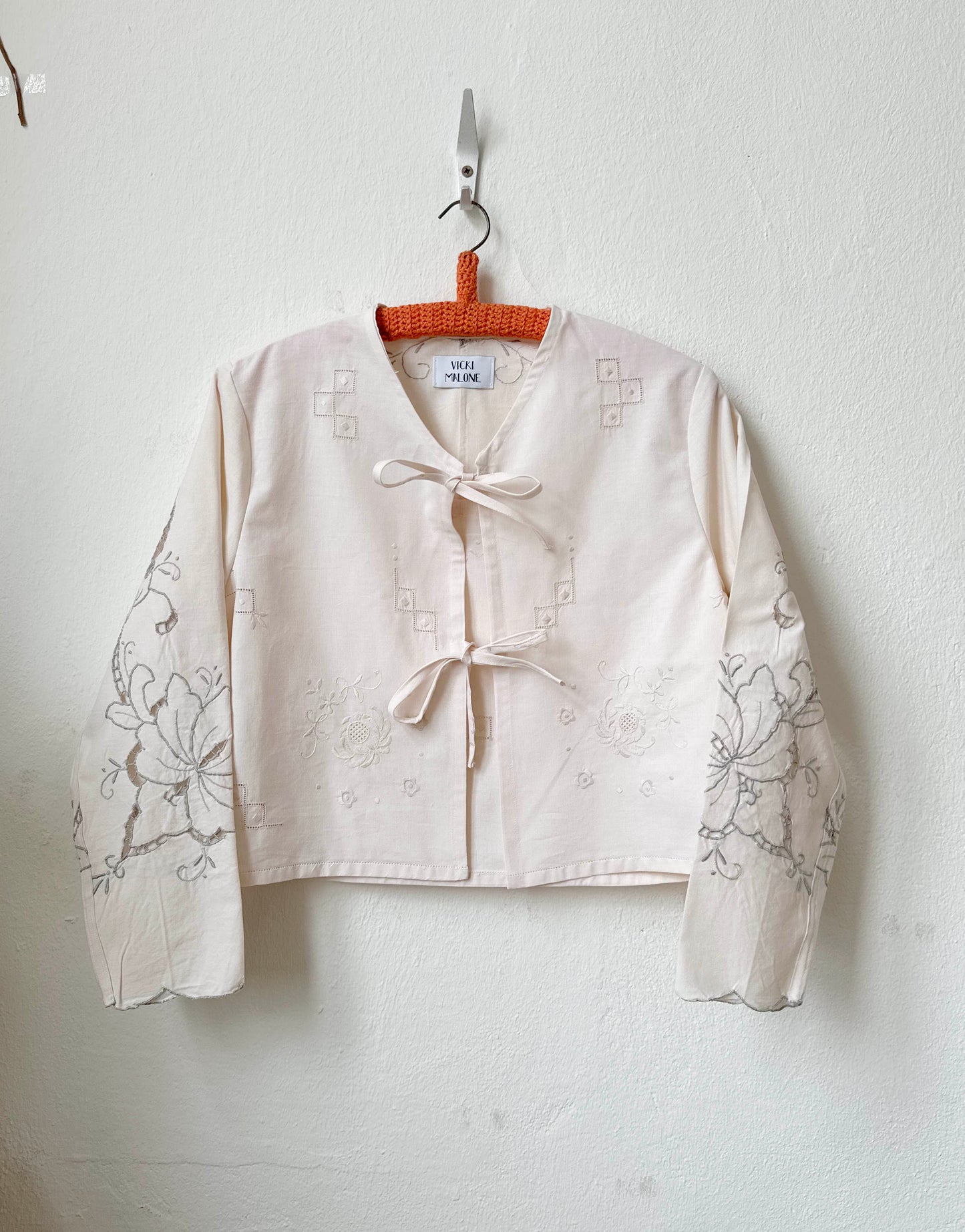 Handmade vintage patchwork embroidered cotton blouse with long sleeves, made from Scottish family tablecloths, hanging on a wall