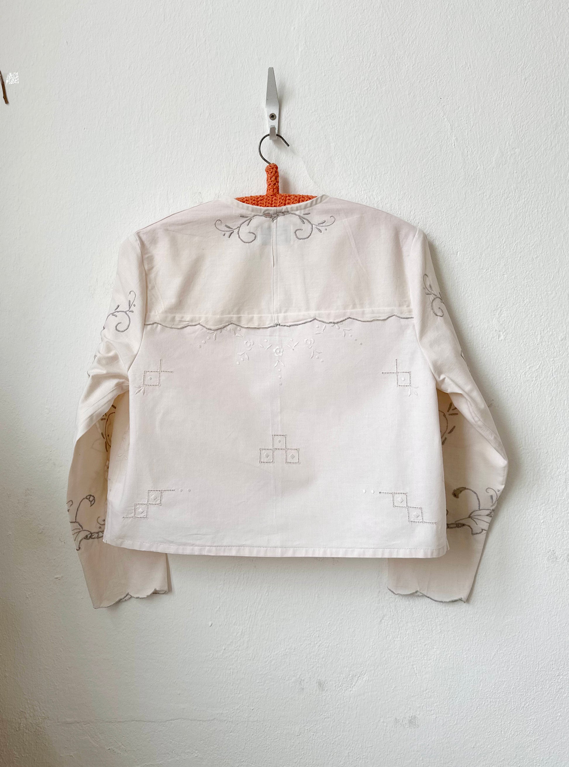 Handmade vintage patchwork embroidered cotton blouse with long sleeves, made from Scottish family tablecloths, hanging on a wall