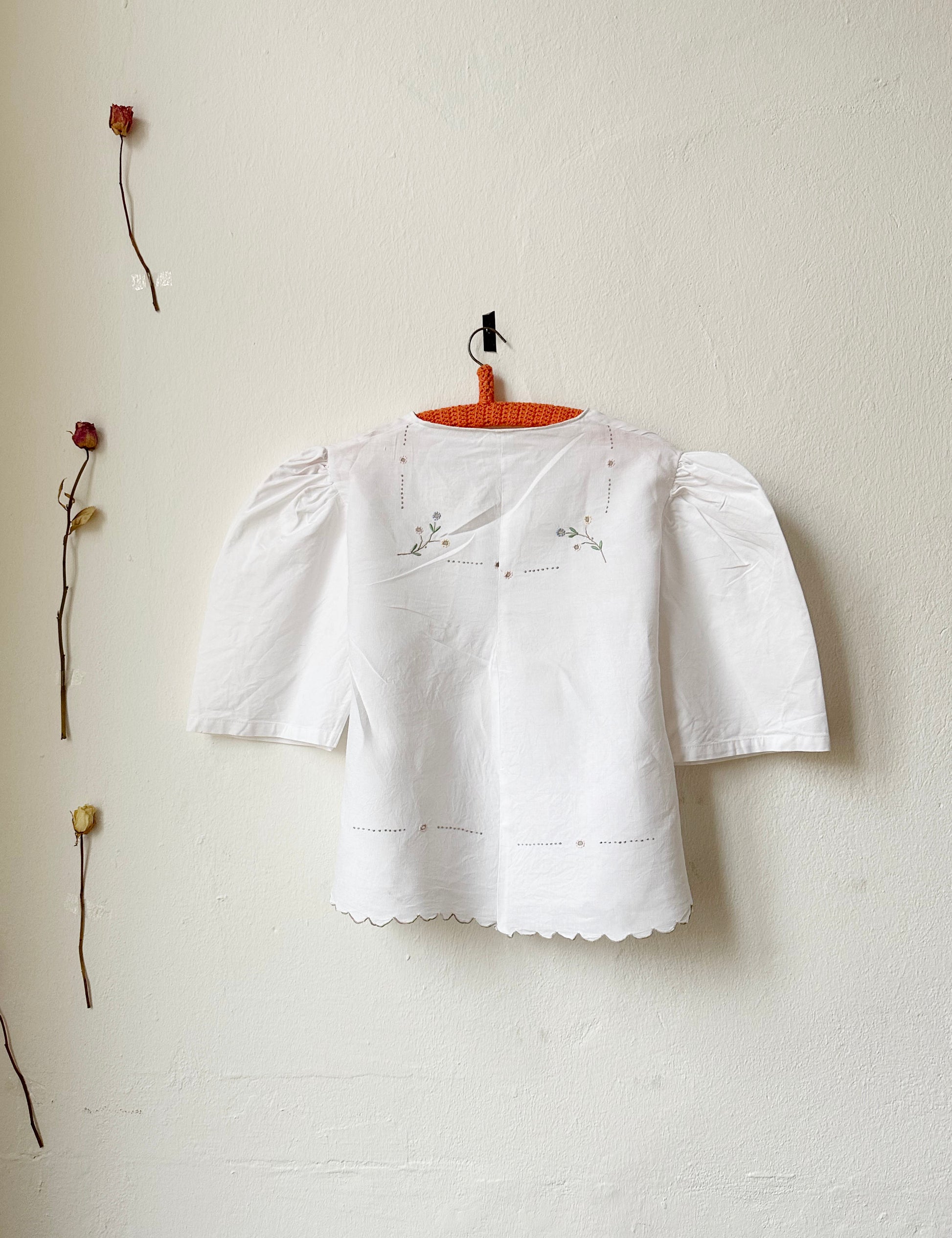 A back view of a white embroidered short sleeve blouse hanging on the wall.
