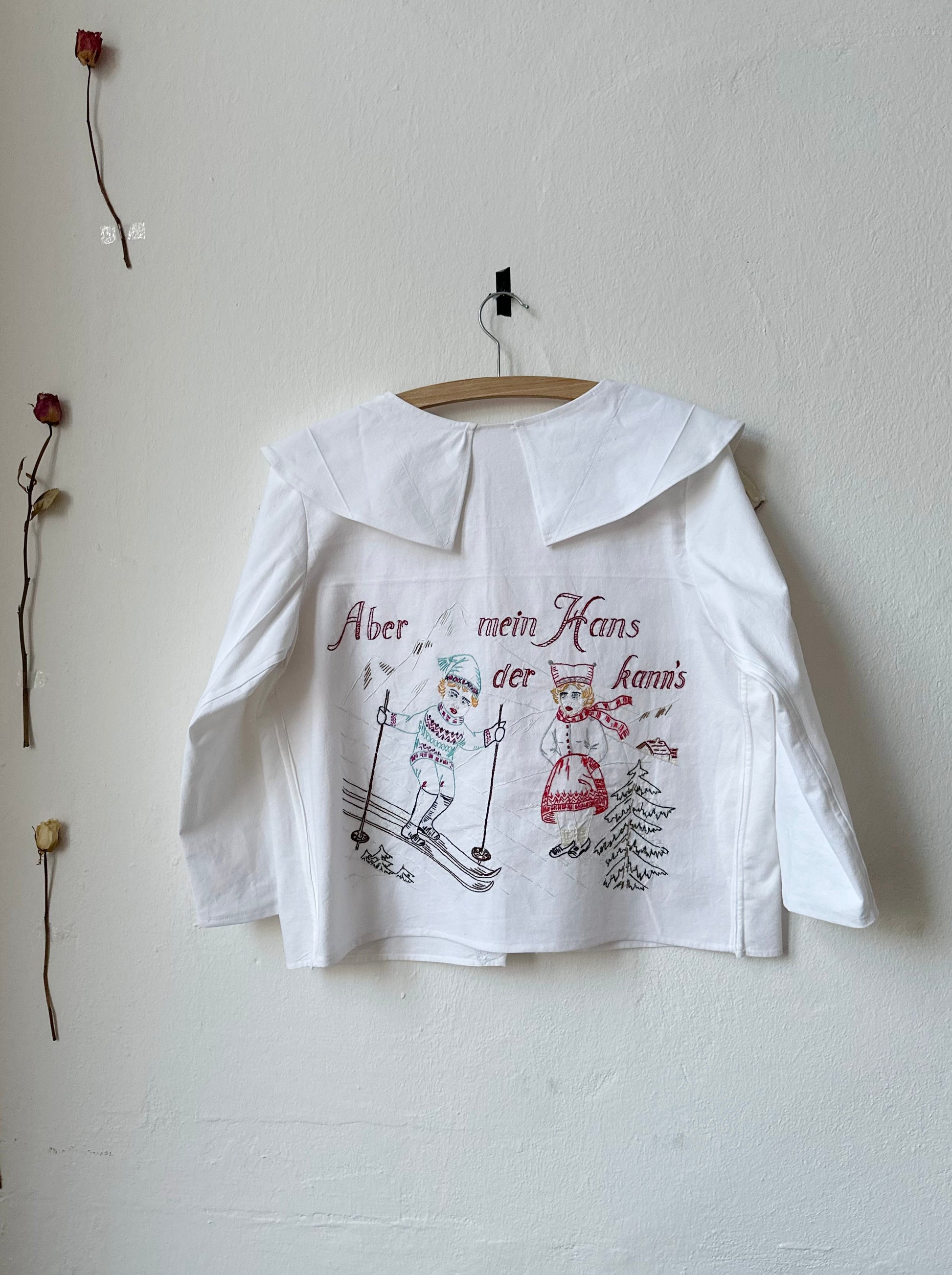 Back view of embroidered white blouse. Embroidery shows a man skiing.