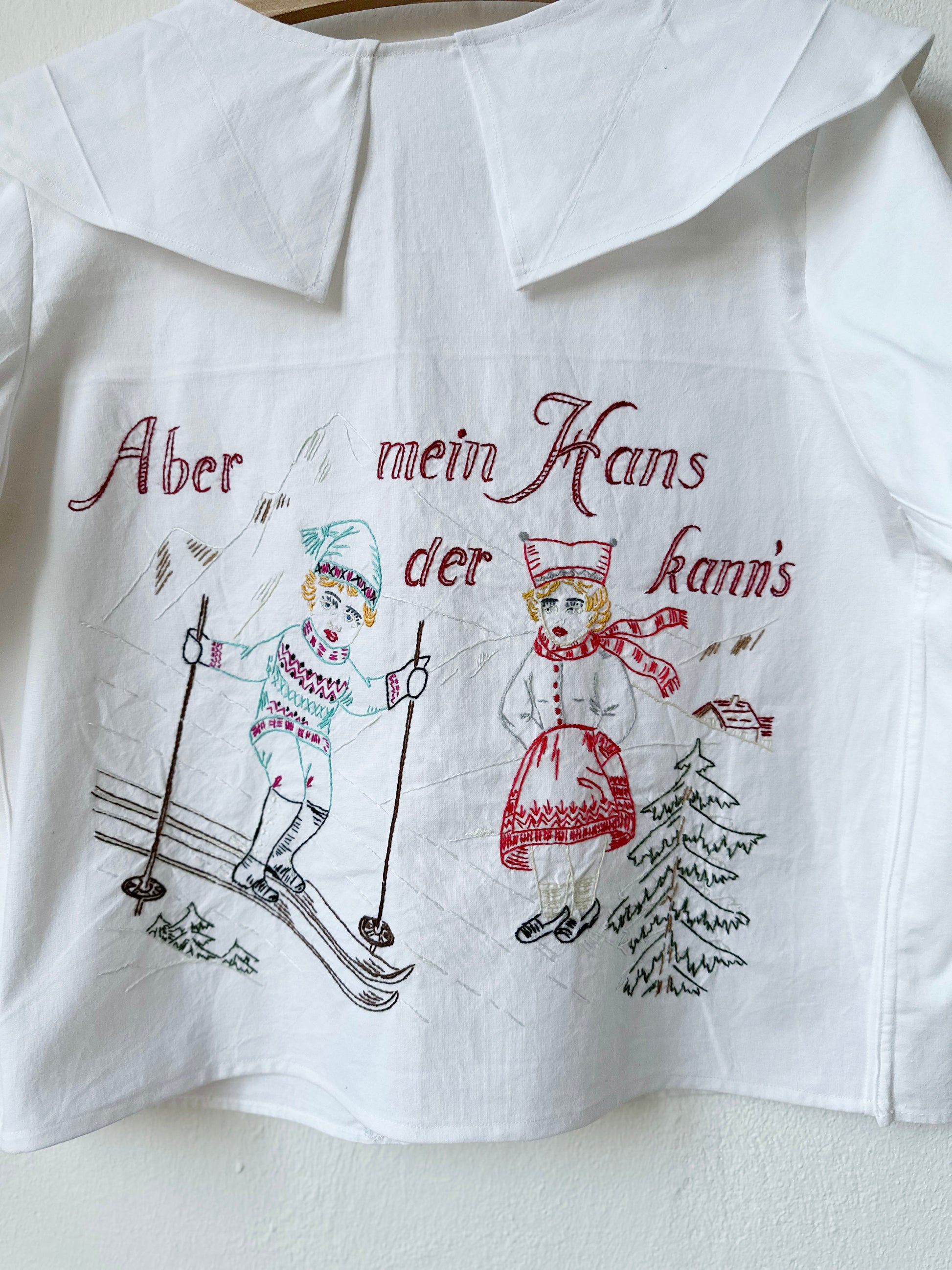 Detail view of back embroidery, words say aber mein Hans der kann's whilst he skis and she watches.