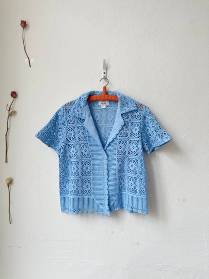 A blue and white check blouse with tie closure and peplum hem hanging on a wall. 