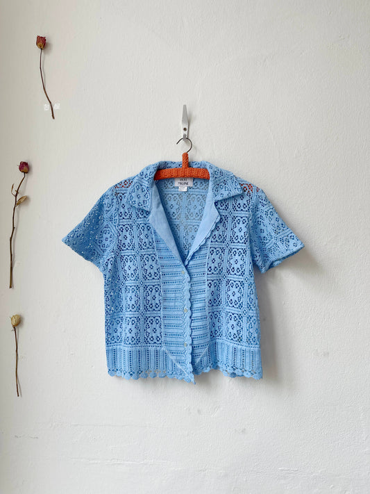A blue and white check blouse with tie closure and peplum hem hanging on a wall. 