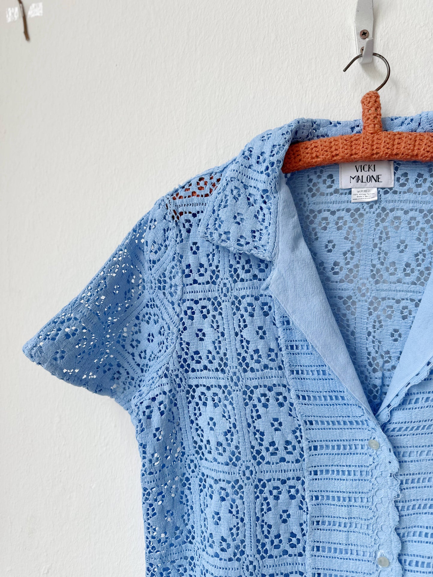 Light blue lace blouse on a hanger against a white background