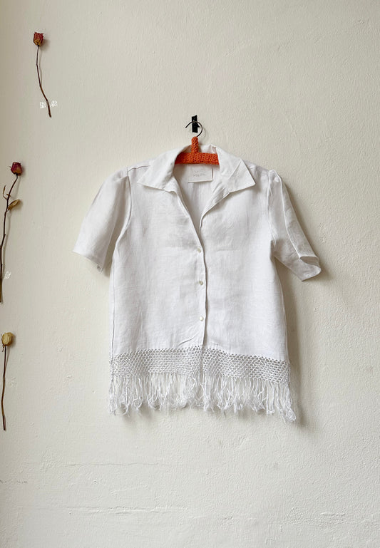 White shirt with fringe hem hangs on a wall.