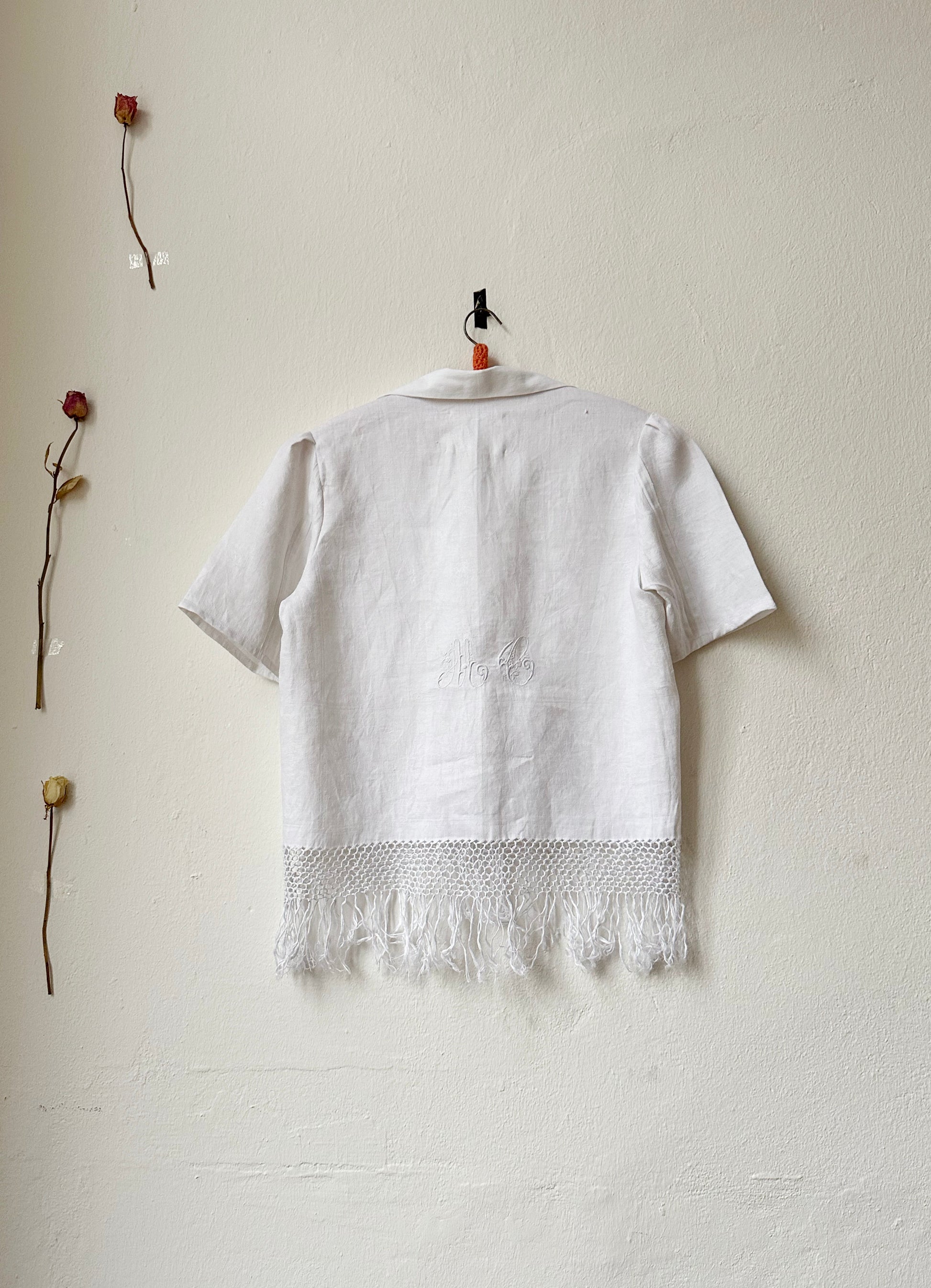 Back view of a white shirt with monogram and fringe hem.