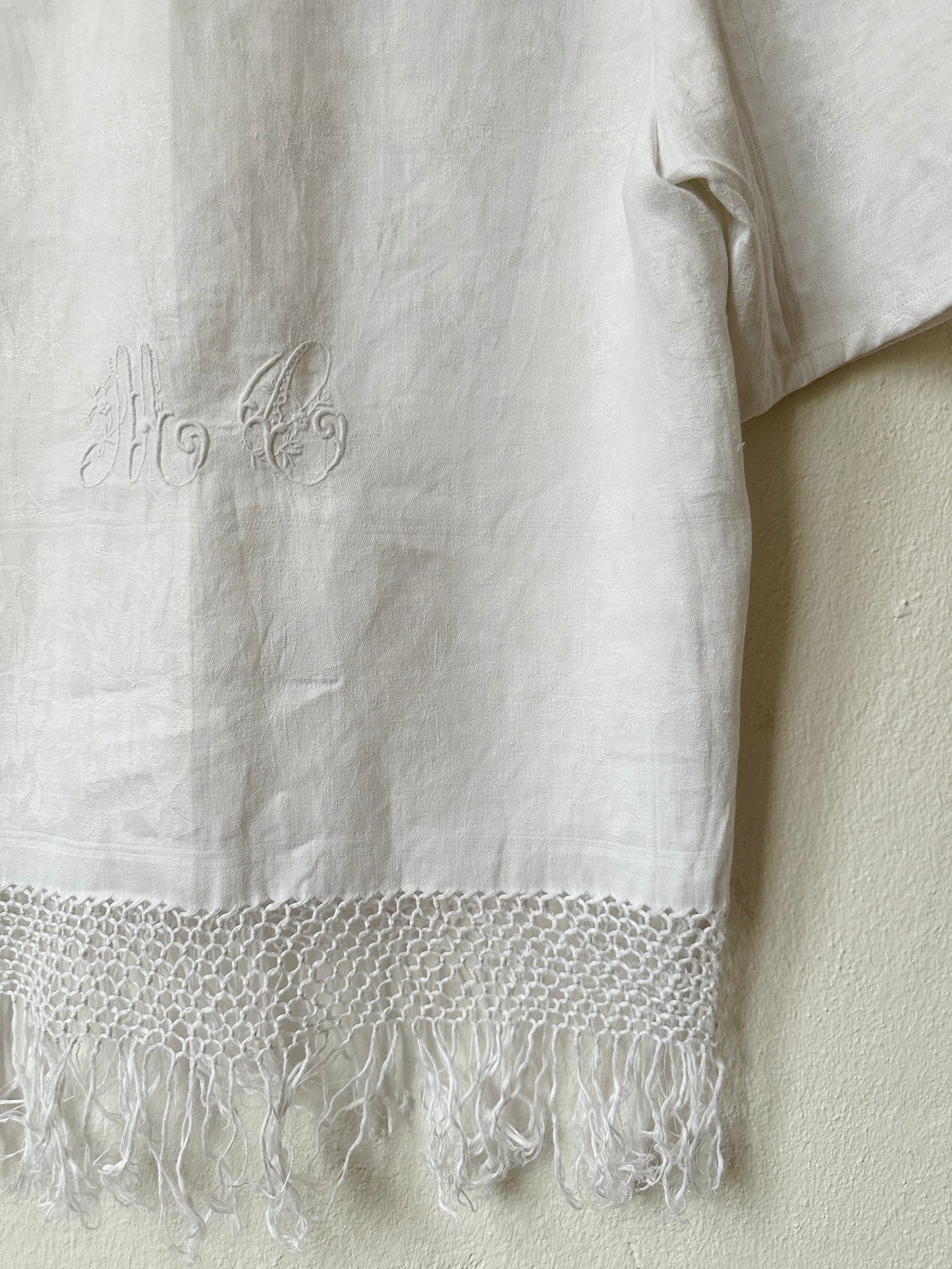 Monogram embroidery detail of a white fringe hem shirt.
