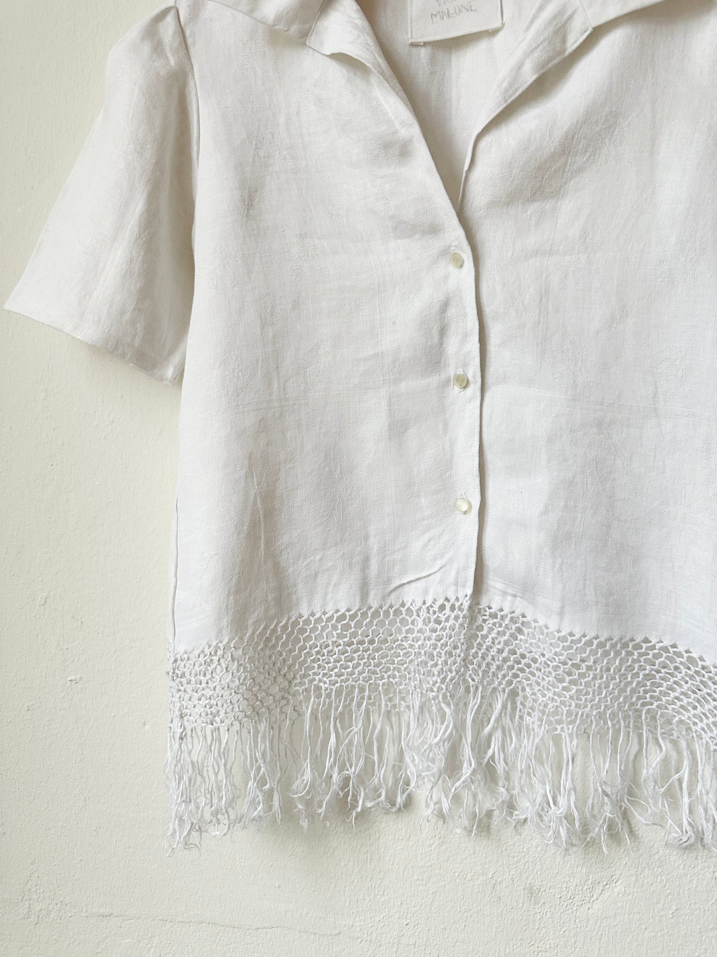 White button front shirt with tassel hem on a white background.