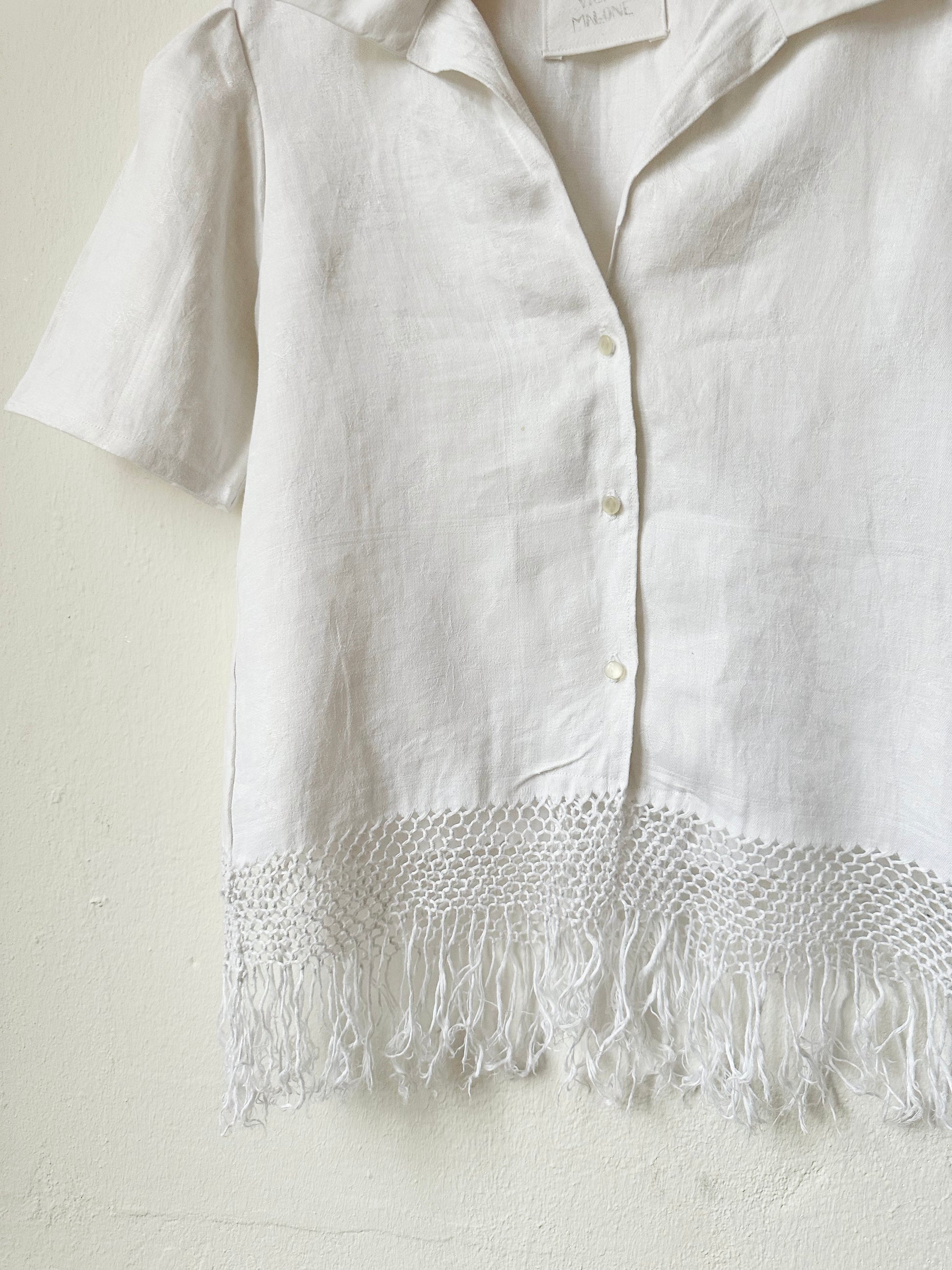 White button front shirt with tassel hem on a white background.