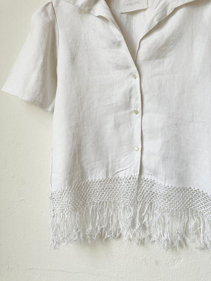 White button front shirt with tassel hem on a white background.