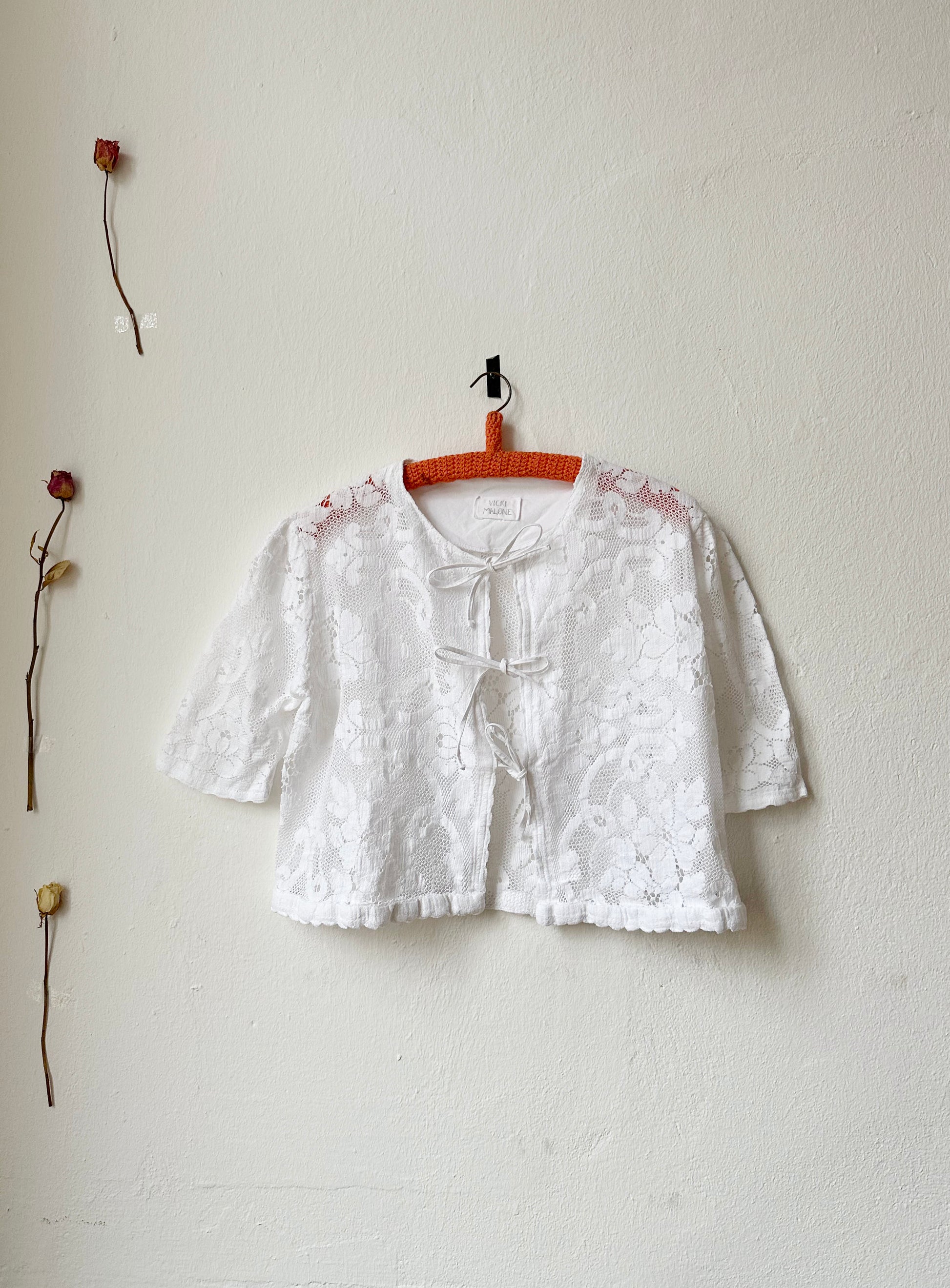 A white floral lace blouse with ties to close front hangs on a wall.