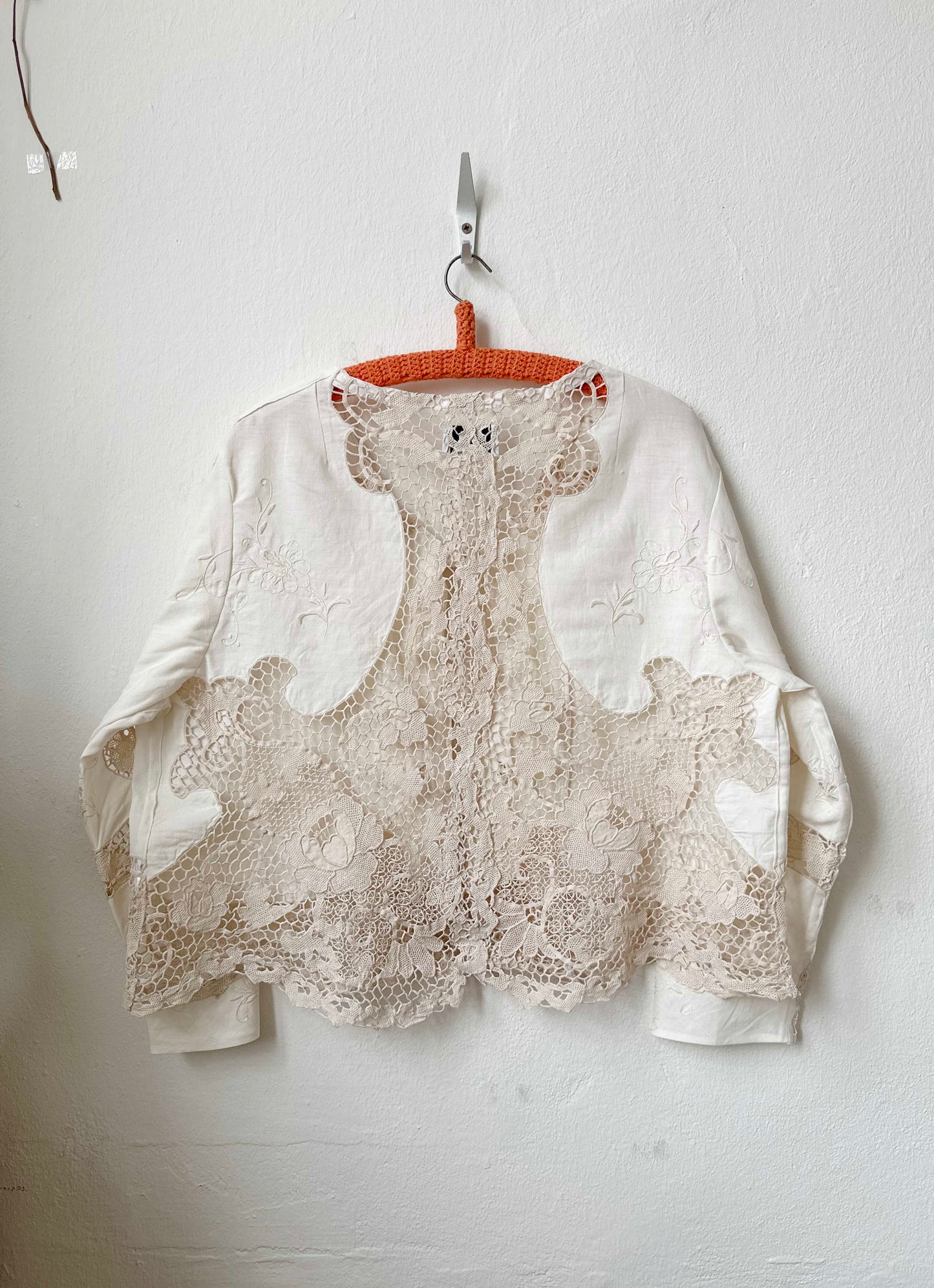 Handmade vintage lace blouse with long sleeves hanging on a wall, made from a Rome flea market tablecloth
