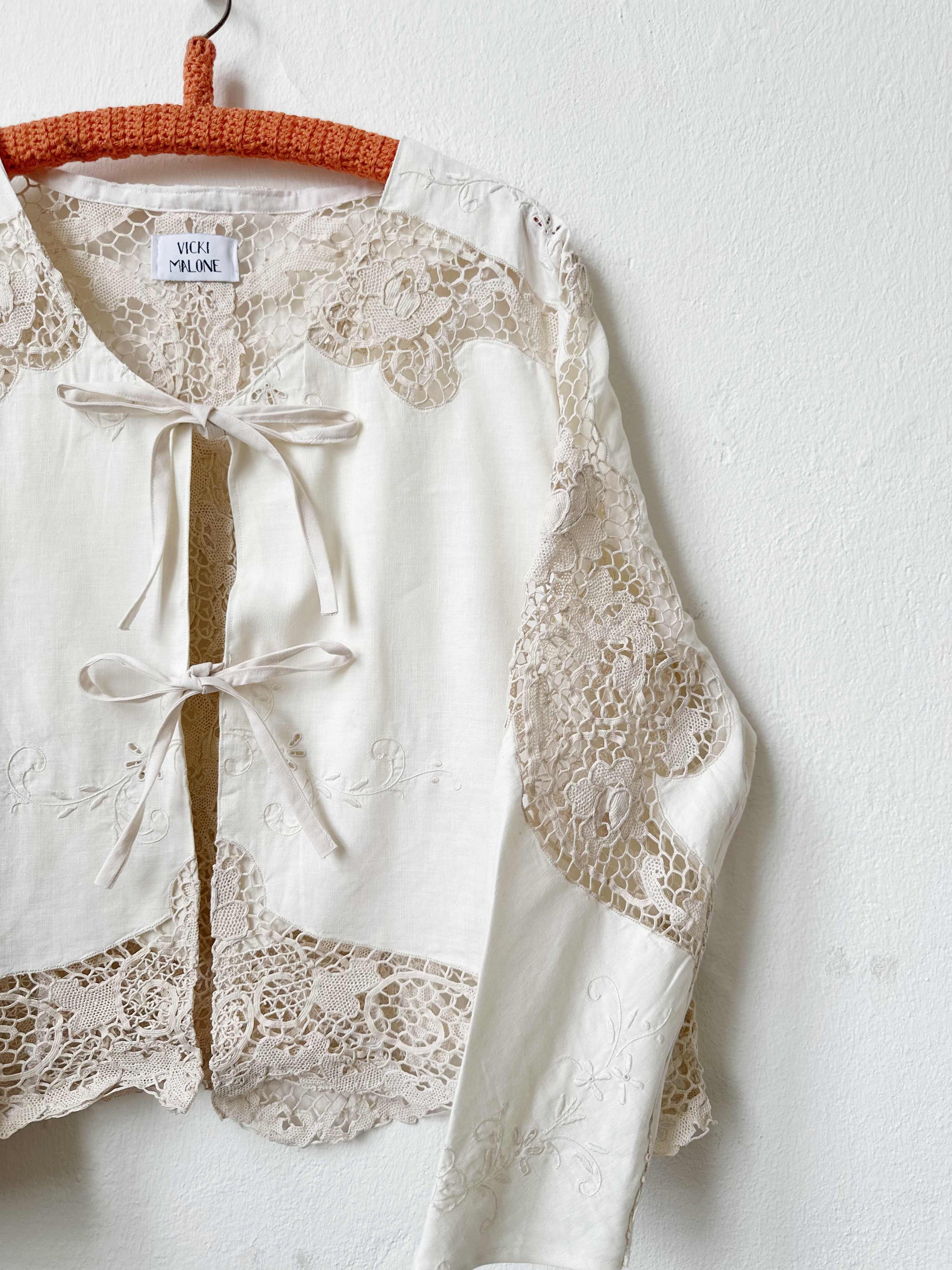 Handmade vintage lace blouse with long sleeves hanging on a wall, made from a Rome flea market tablecloth
