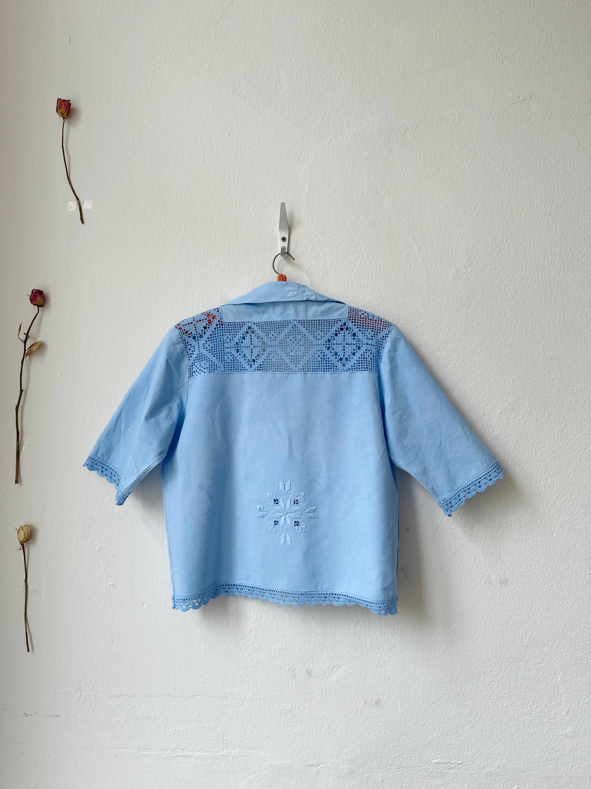 Light blue embroidered shirt hanging on a white wall with dried flowers.