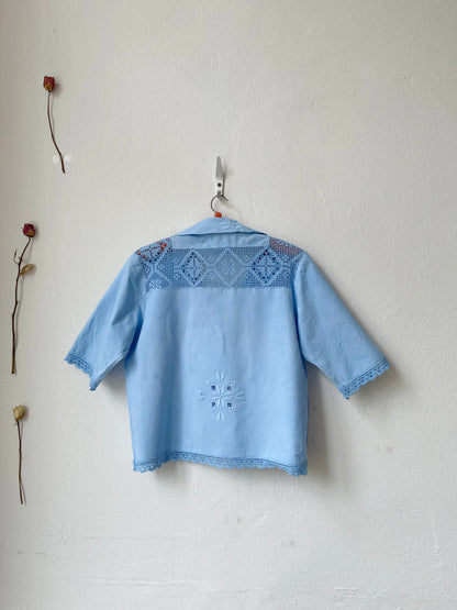 Light blue embroidered shirt hanging on a white wall with dried flowers.