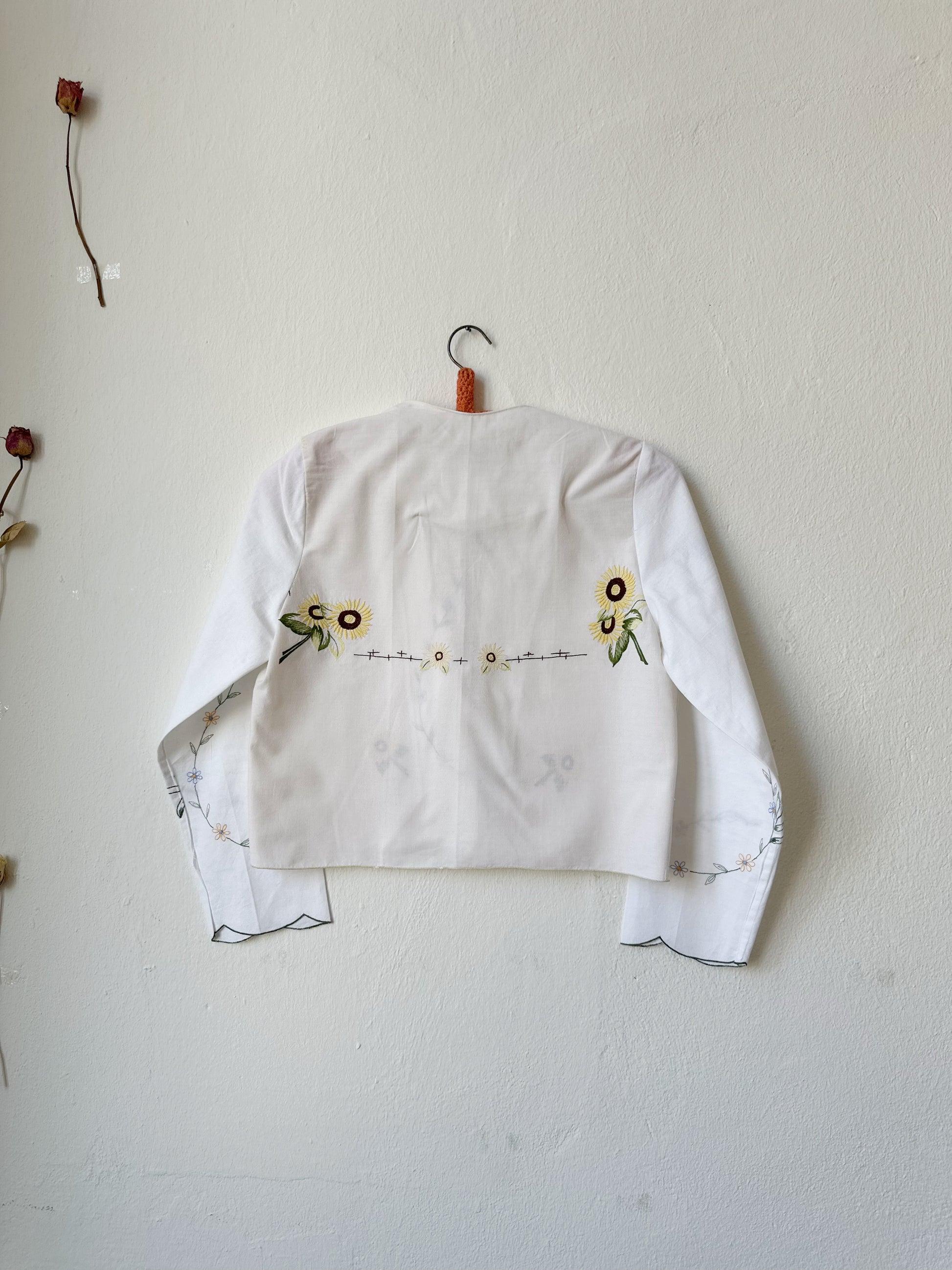 The back view of a patchworked floral embroidered long sleeve blouse hanging on a wall.