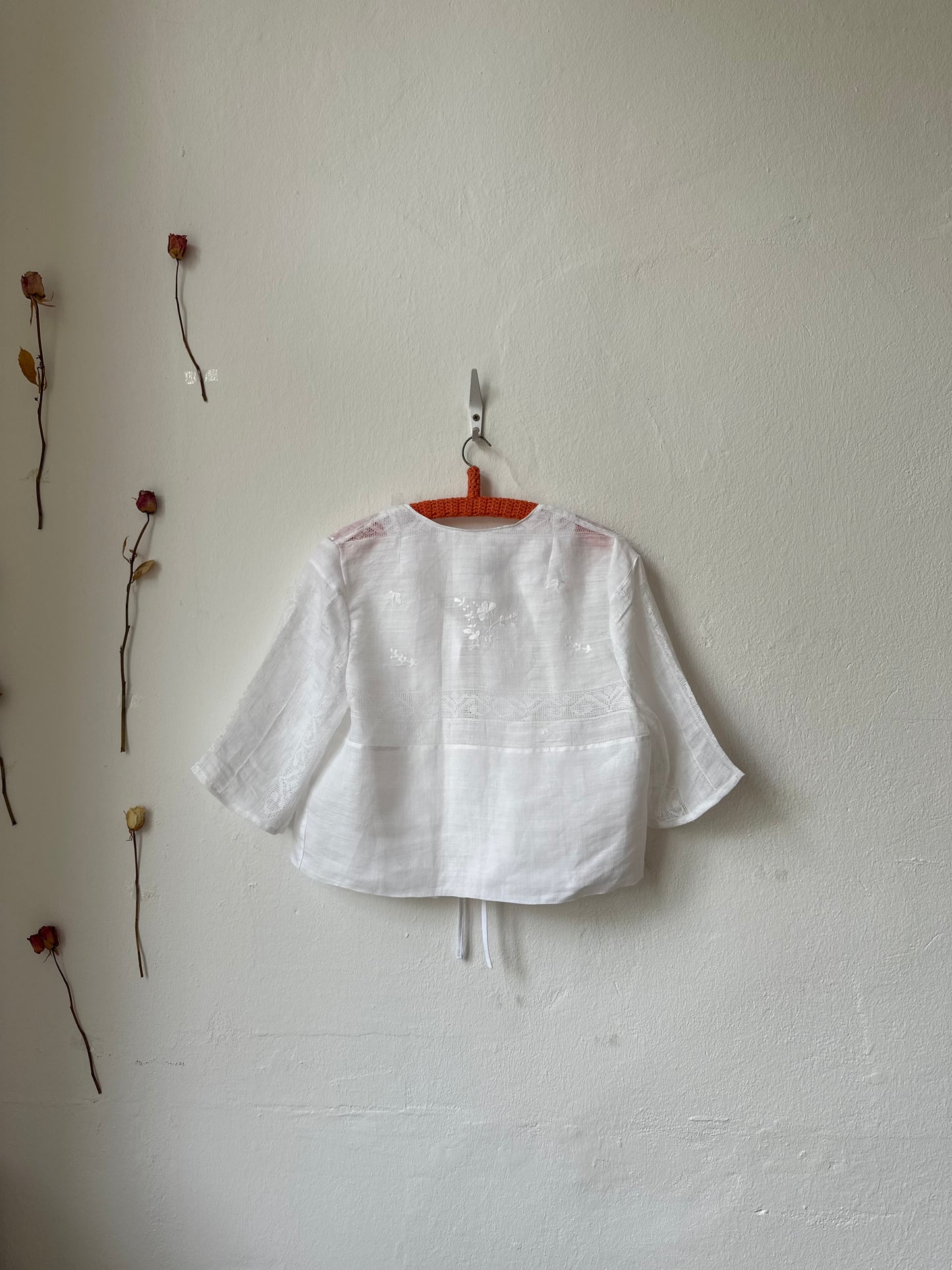 White shirt hanging on a hook against a white wall with dried plants.